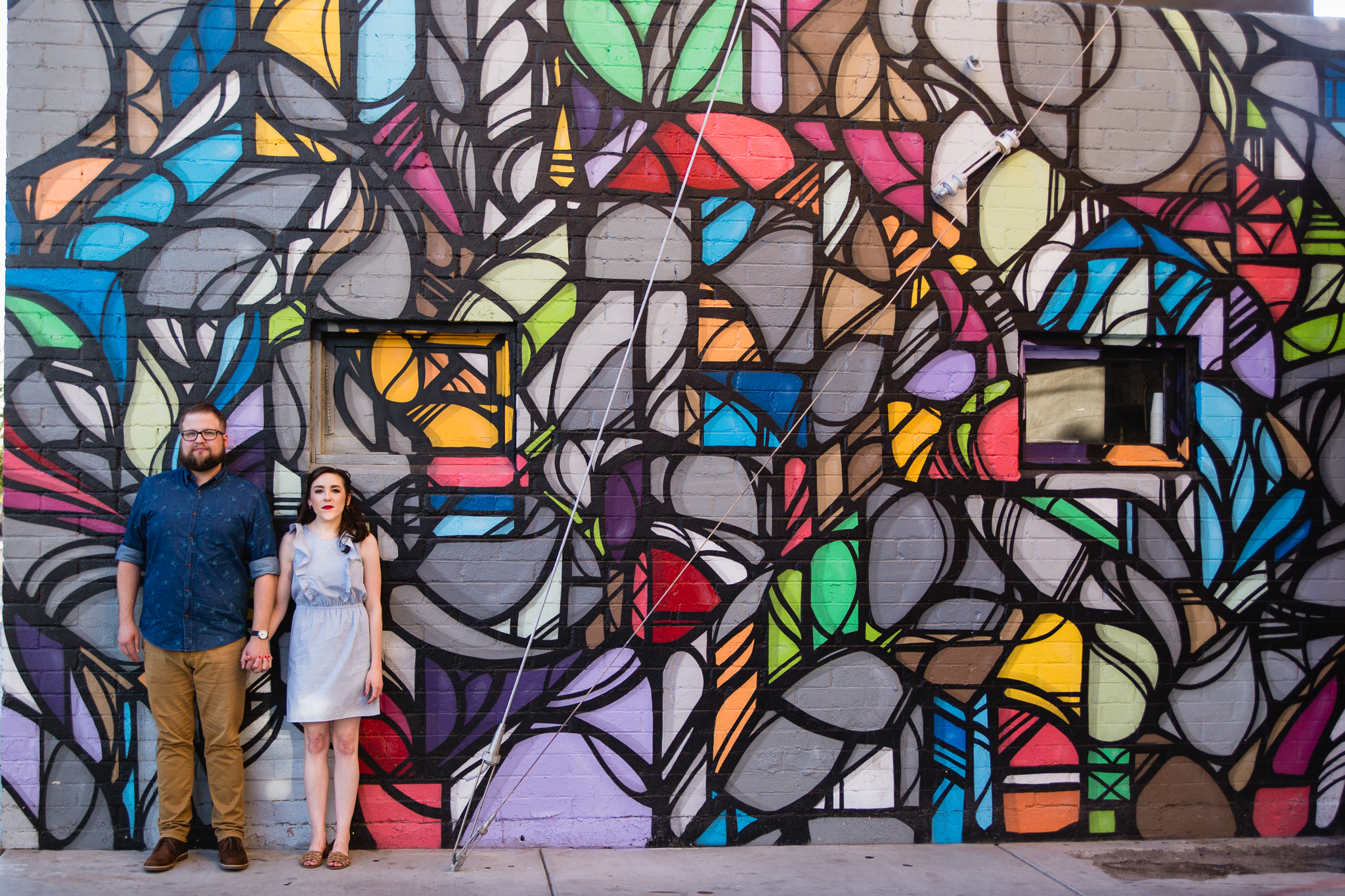 Couple posing in front of art mural during their urban engagement session by Phoenix engagement photographer PMA Photography.