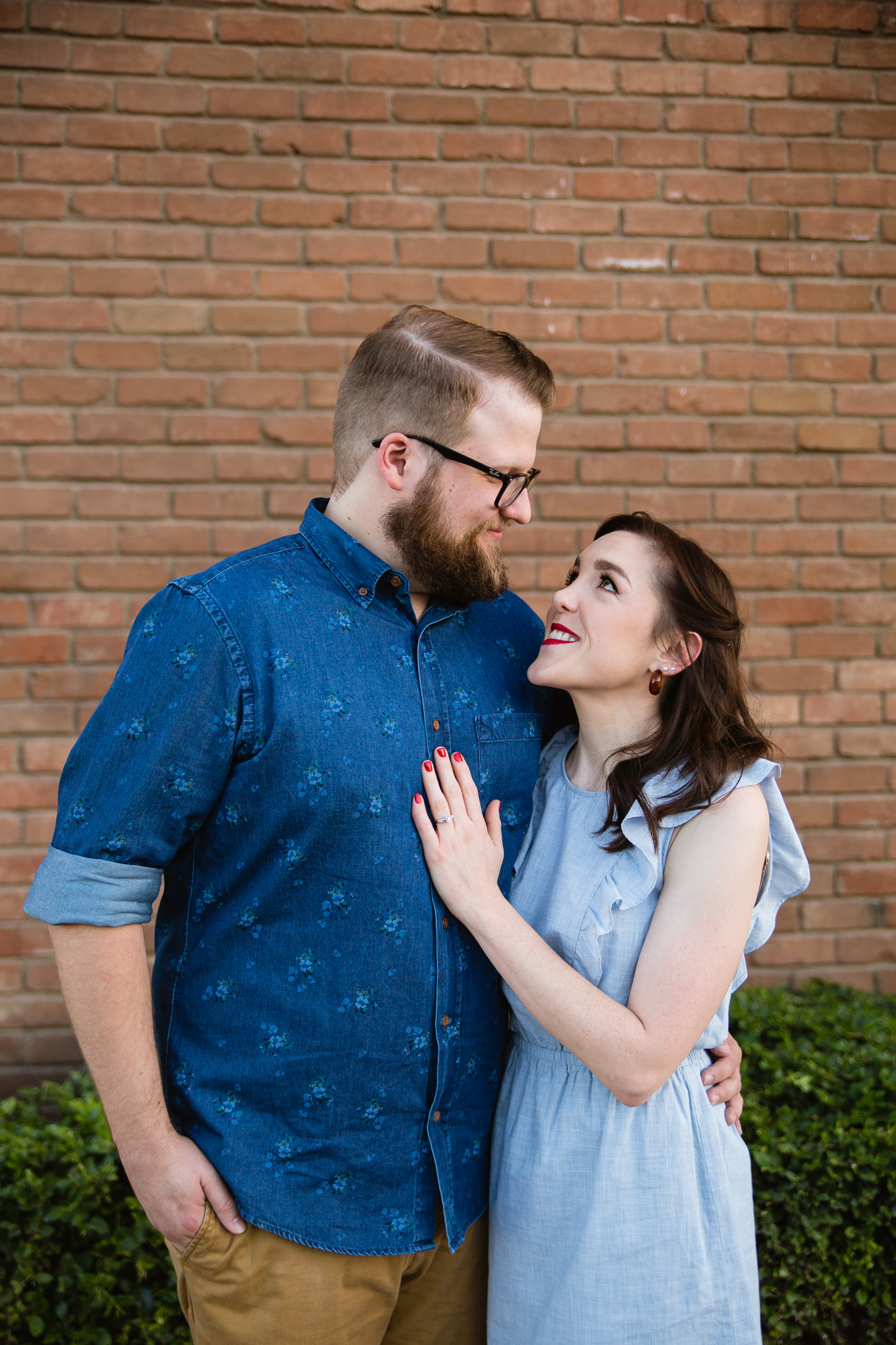 Couple looking at each other in front of red brick wall during their urban engagement session by Phoenix engagement photographer PMA Photography.