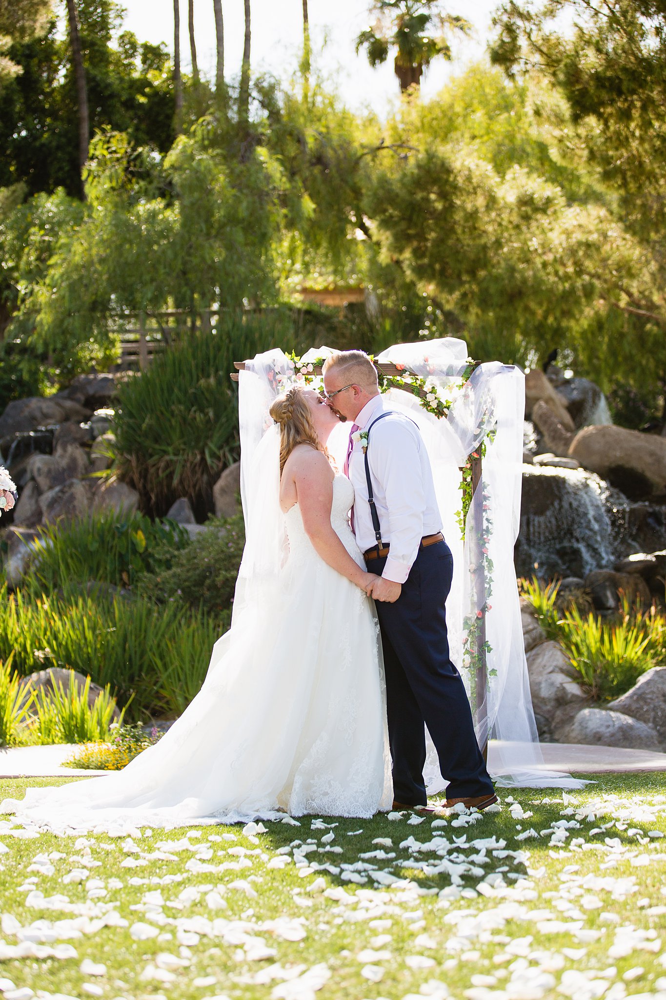 Bride and groom share their first kiss during their wedding ceremony at Val Vista Lakes by Arizona wedding photographer PMA Photography.