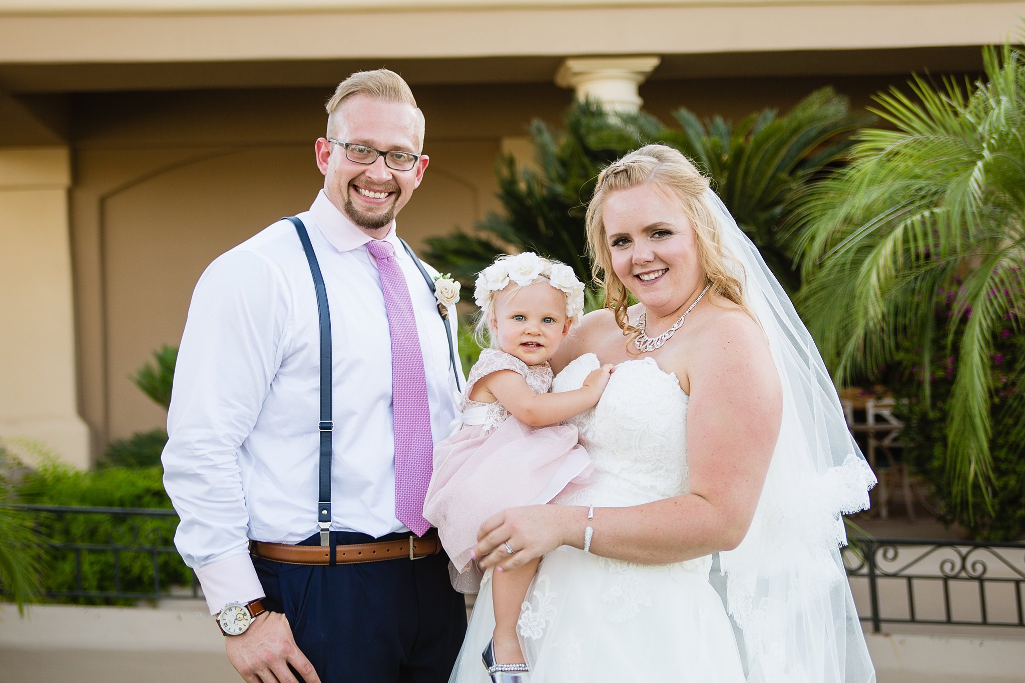 Bride and groom pose with their daughter during their Val Vista Lakes wedding by Arizona wedding photographer PMA Photography.