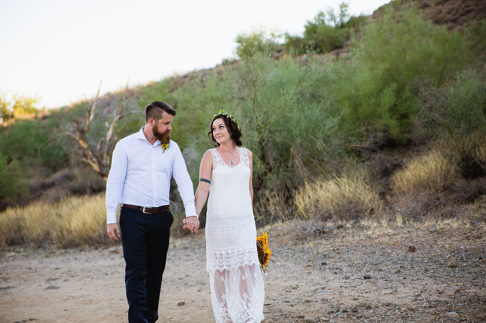 Simple boho inspired bride and groom walk together through the Arizona desert by Phoenix wedding photographer PMA Photography.