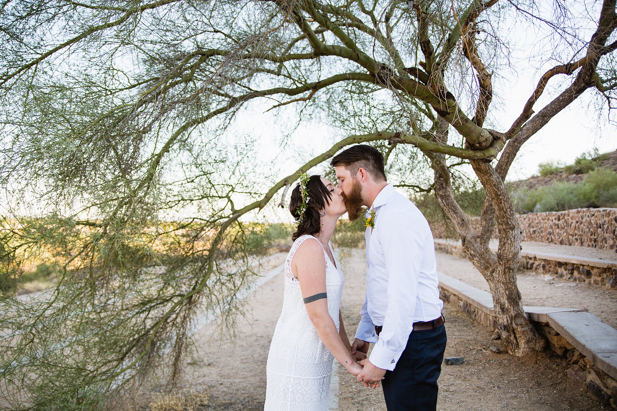 Simple boho inspired bride and groom share a kiss under a tree by Arizona wedding photographers PMA Photography.