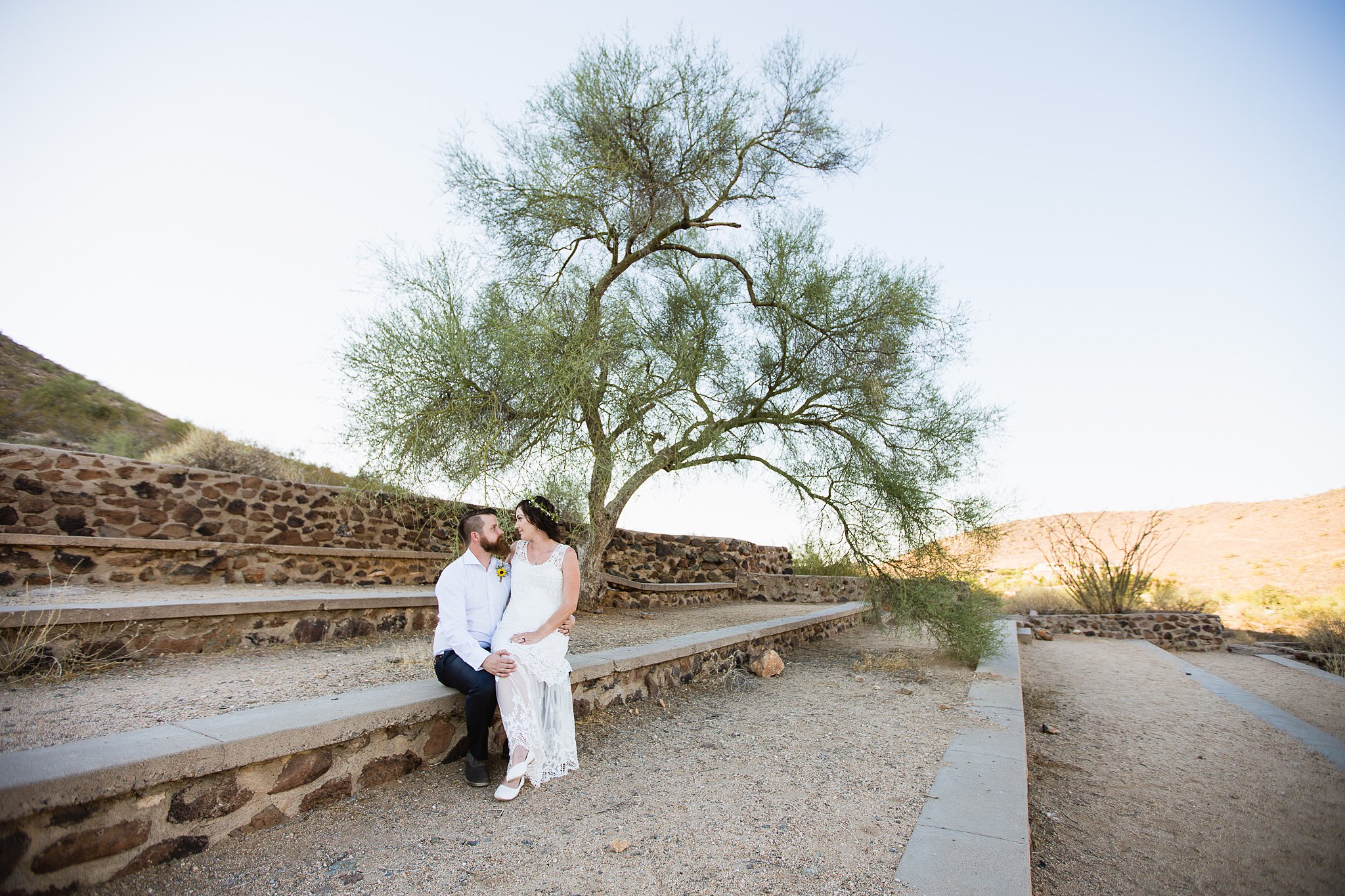Bride and groom look at each other under a desert tree by Phoenix wedding photographer PMA Photography.