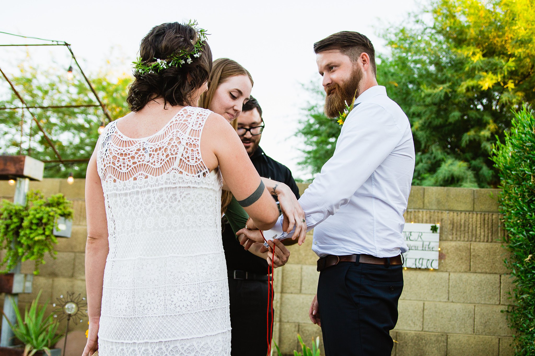 Bride and groom during their red chord handfasting ceremony as part of their wedding ceremony by Arizona wedding photographer PMA Photography. 