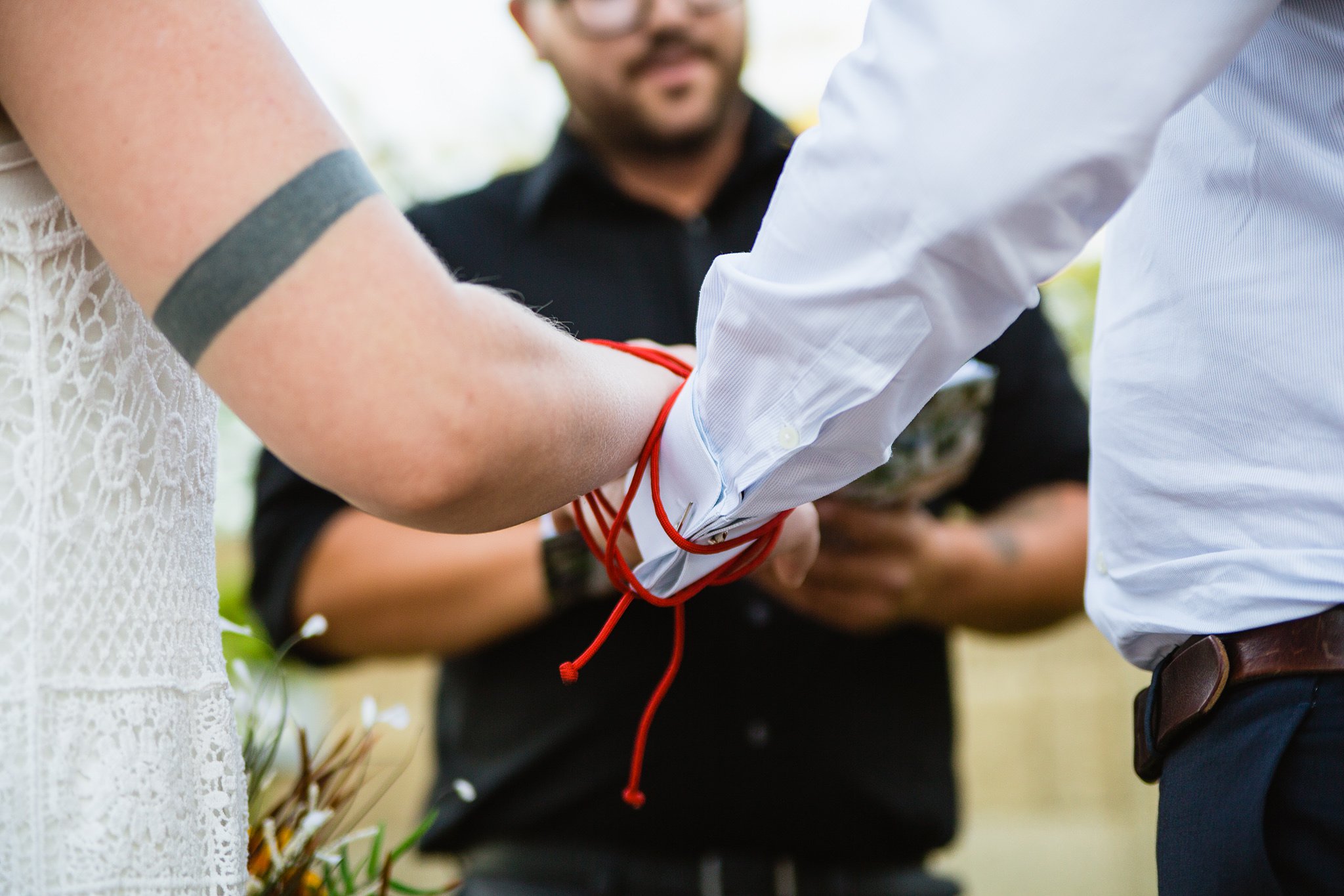 Bride and groom's hands tied together during a Celtic red chord handfasting ceremony by Phoenix wedding photographer PMA Photography.