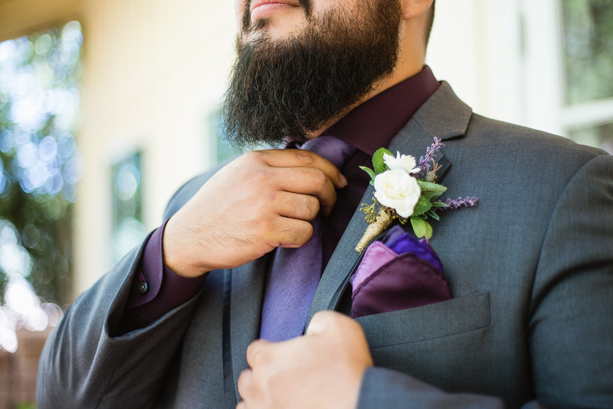 Groom adjusting the tie on his purple and grey suit while getting ready for his wedding day by Phoenix wedding photographers PMA Photography.