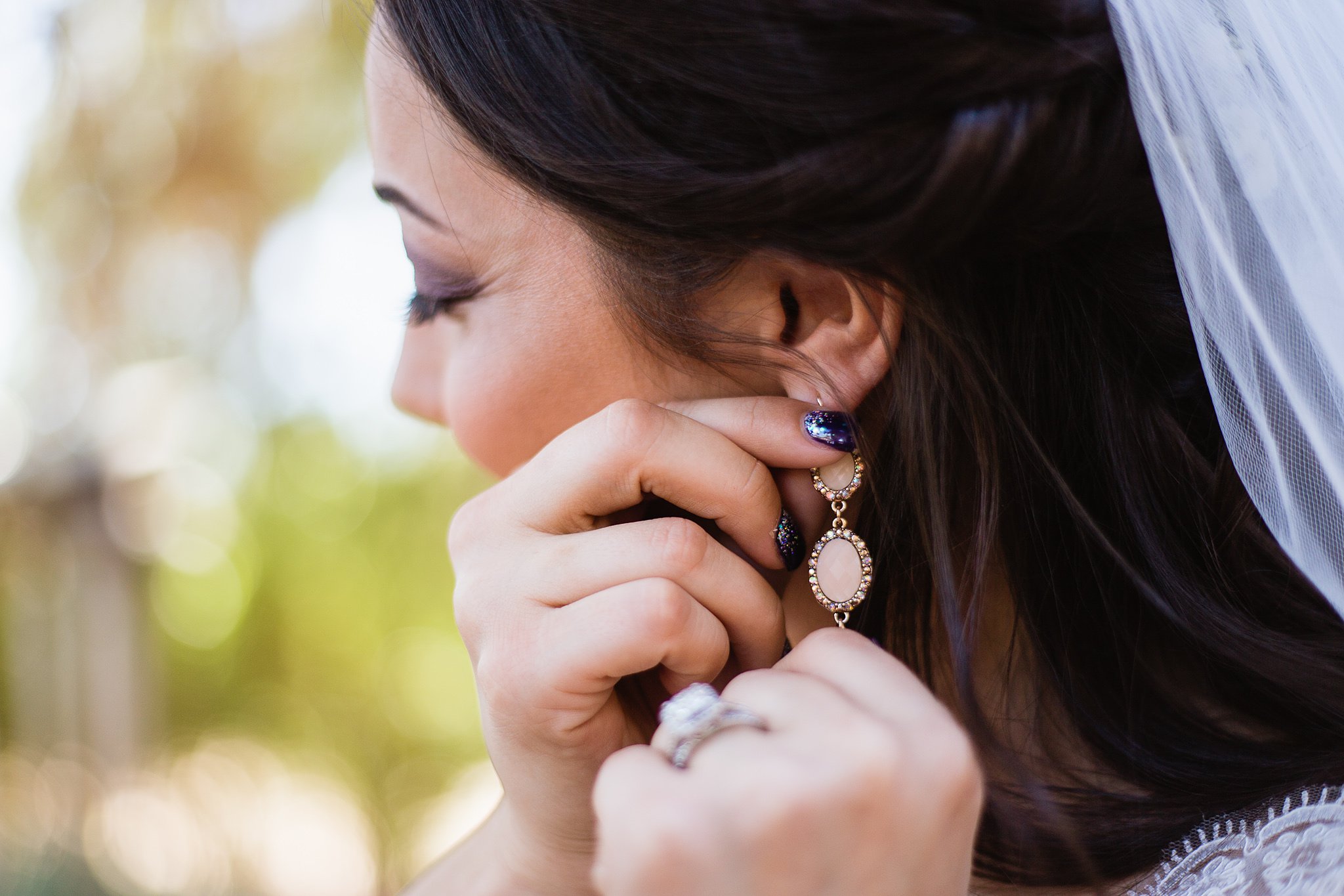 Bride adjusting her pink and rose gold earring while getting ready by Arizona wedding photographer PMA Photography.