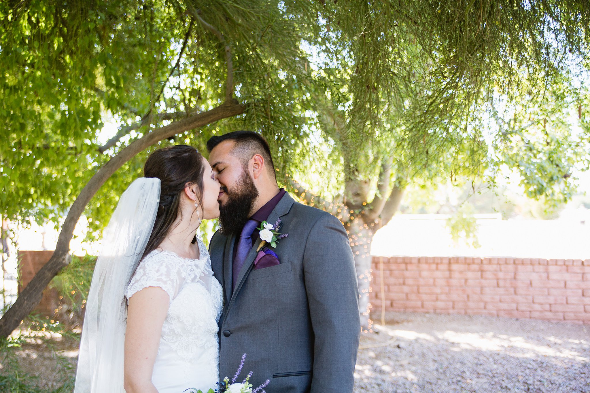 Bride and groom share a kiss in front of trees at wedding at Schnepf Farm's Farmhouse by Phoenix wedding photographers PMA Photography.