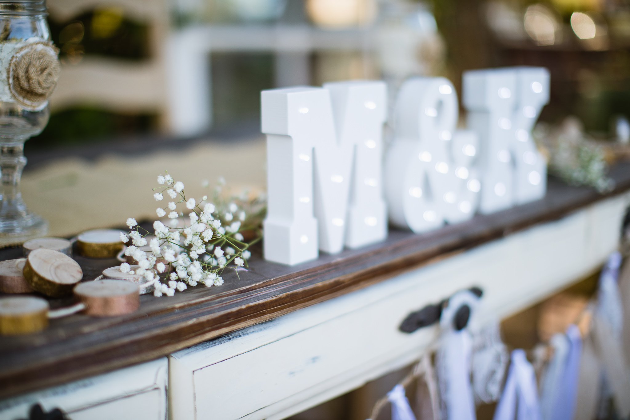 Rustic chic wedding reception decorations of wood slices, babies breath, and couples initials by Arizona wedding photographers PMA Photography.