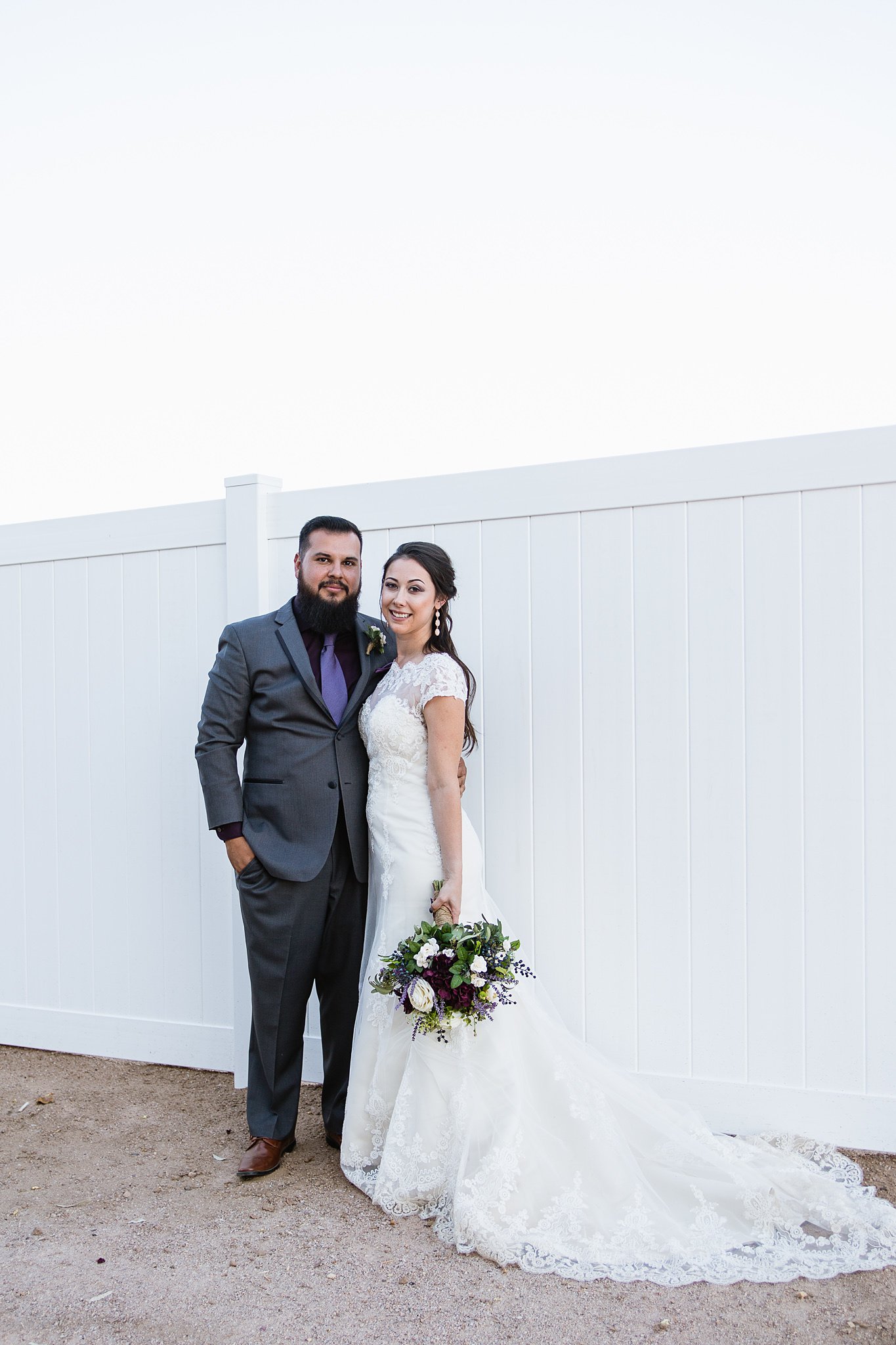 Bride and groom pose in front of white wall for their grey and purple rustic chic wedding at Schnepf Farms Farmhouse by PMA Photography. 