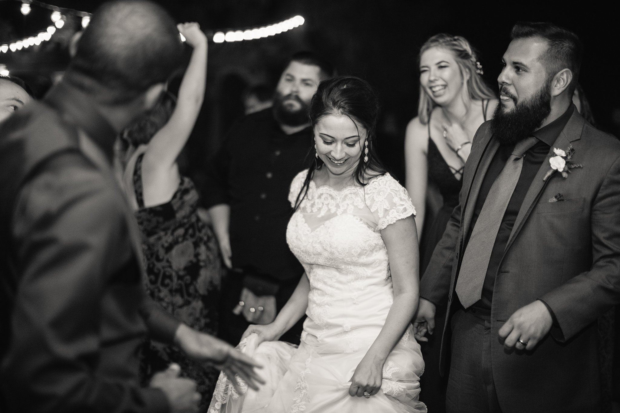 Black and white image of bride and groom having fun dancing with guests at wedding reception by Arizona wedding photographer PMA Photography.