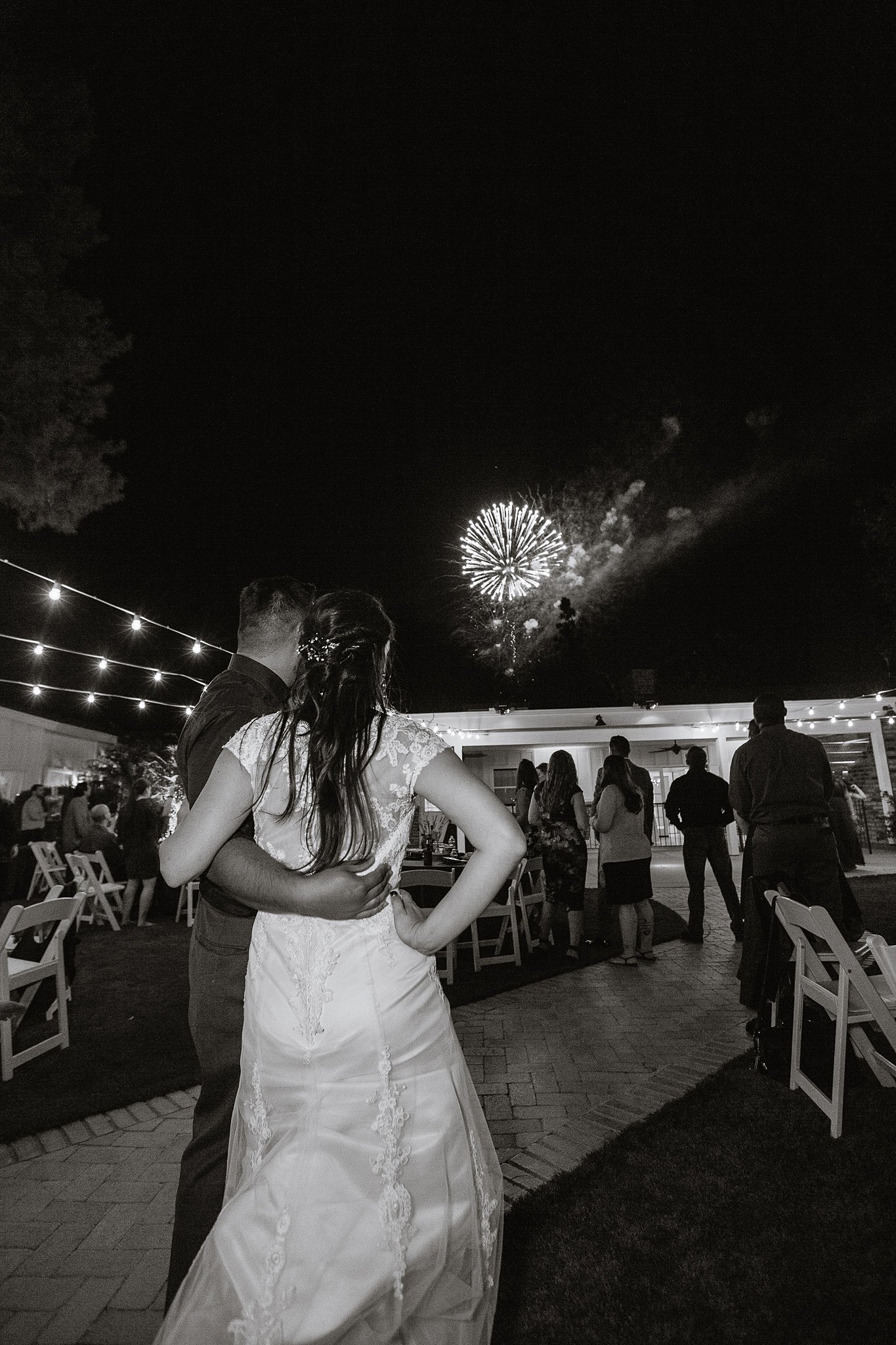 Black and white image of Bride and groom watch fireworks with guests at their wedding reception at Schnepf Farms by Phoenix wedding photographer PMA Photography.