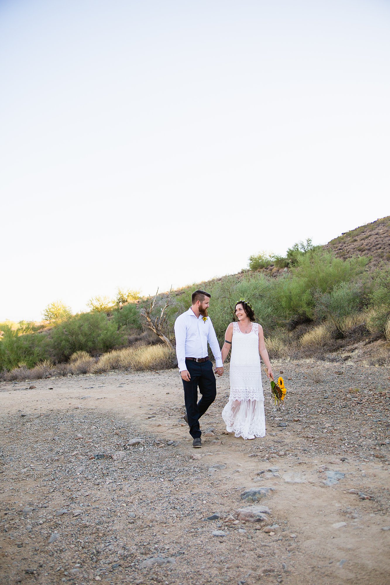 Simple boho bride and groom walking in the Arizona desert by Phoenix wedding photographers PMA Photography.
