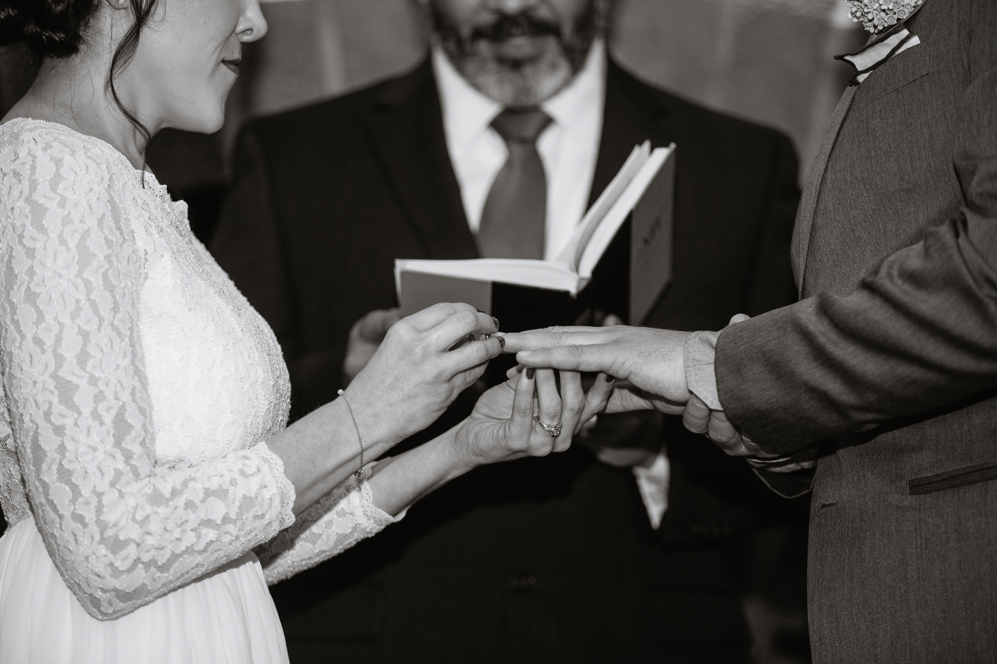 Black and White image of a bride putting a ring on the grooms ring during the wedding ceremony.