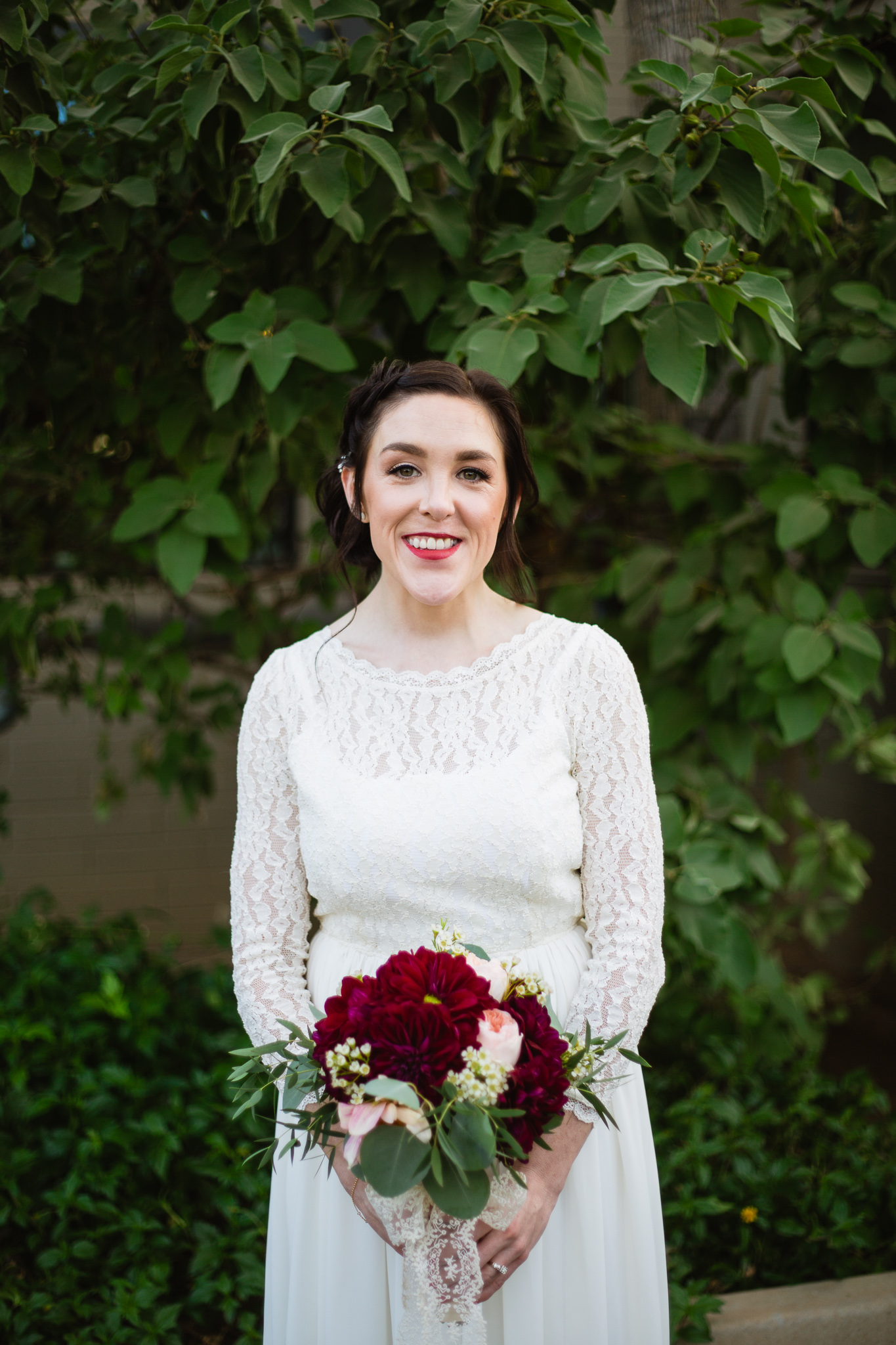 Classic vintage bride portrait in front of green plants with maroon and pink bouquet.