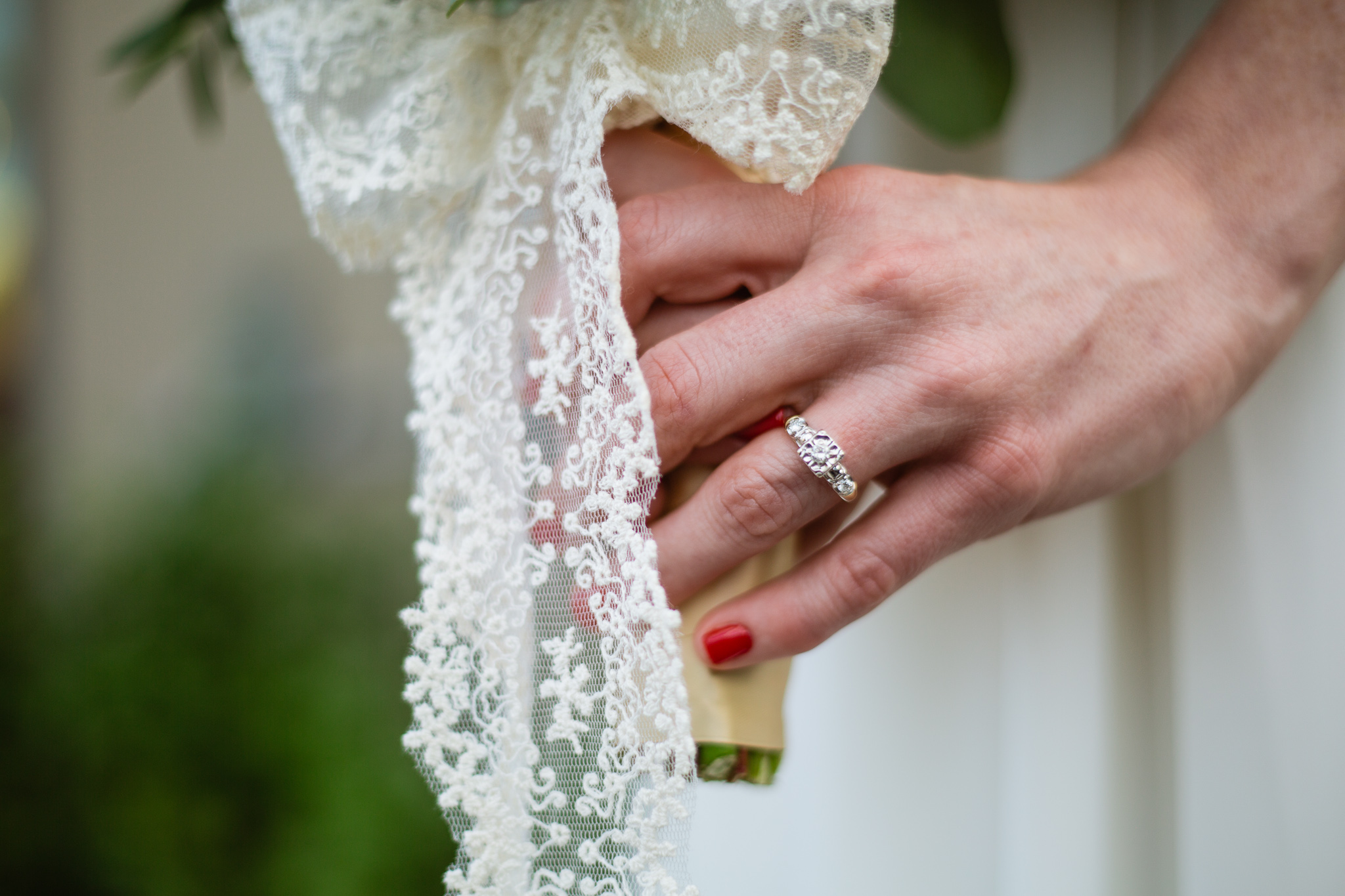 Wedding details of a bride's engagement ring holding her bouquet with lace.