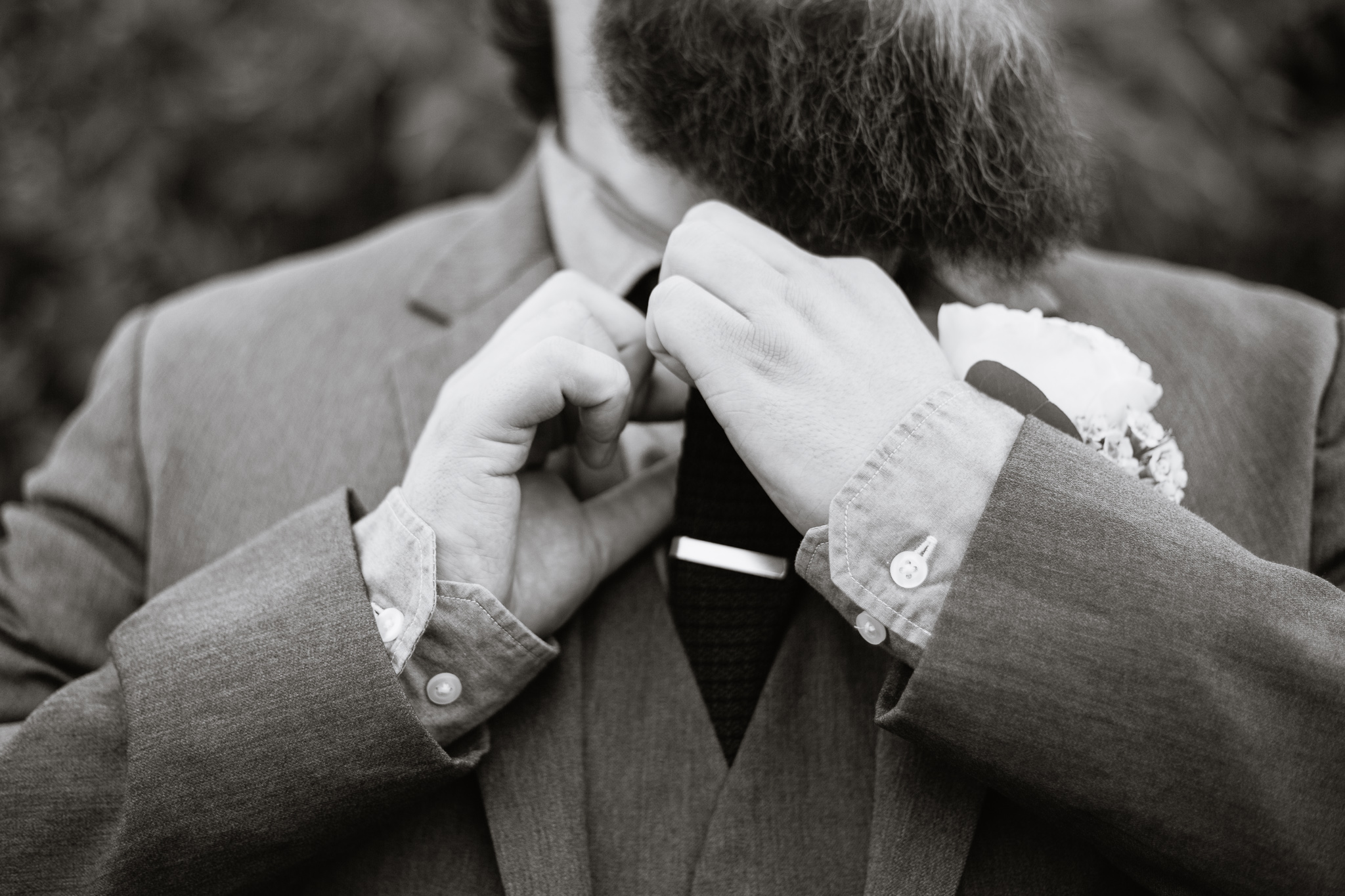 Black and white image of a groom adjusting his tie while getting ready for his wedding day.