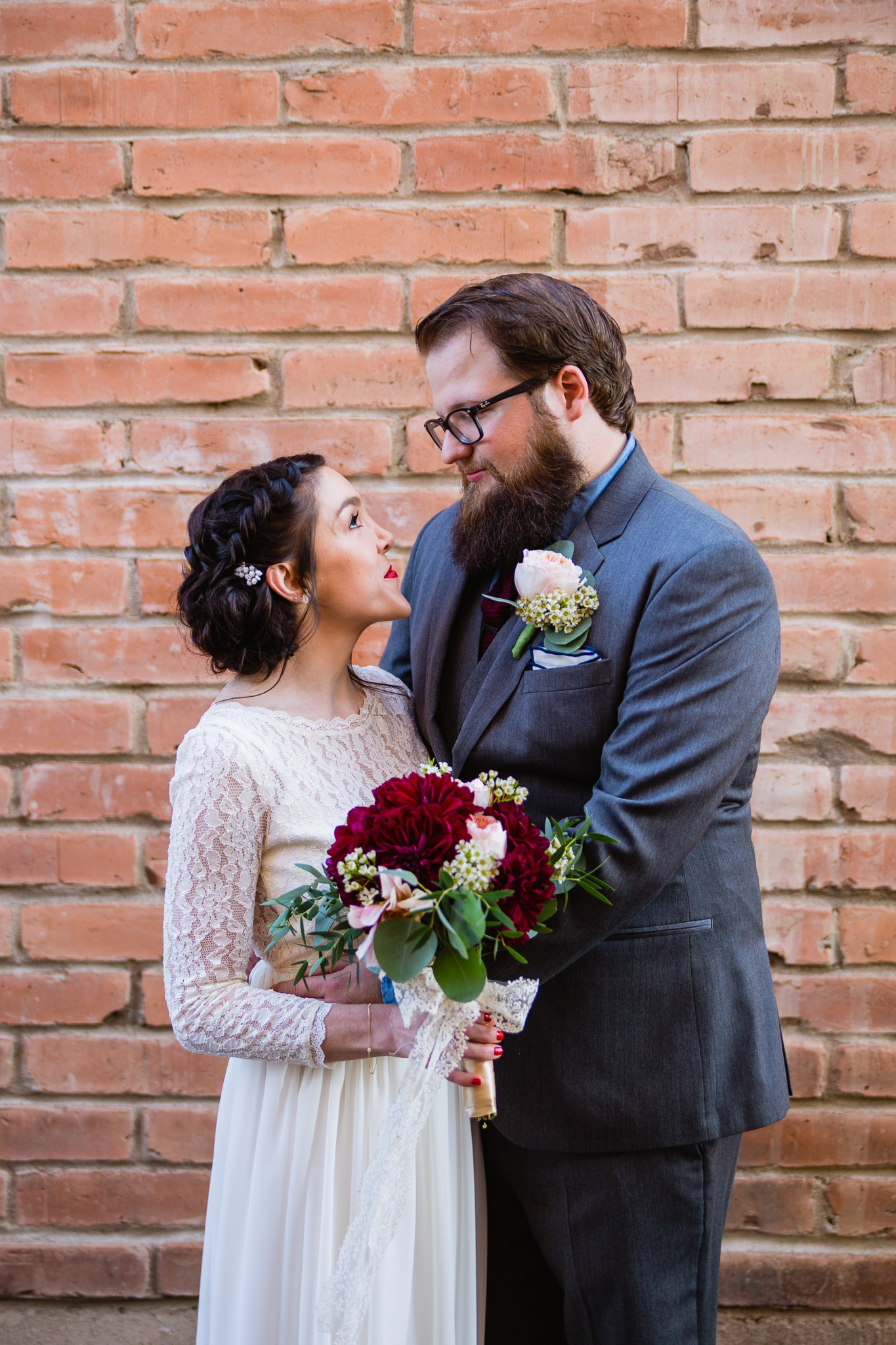 Vintage inspired bride and groom in front of brick wall from a maroon and cream wedding in downtown Phoenix.