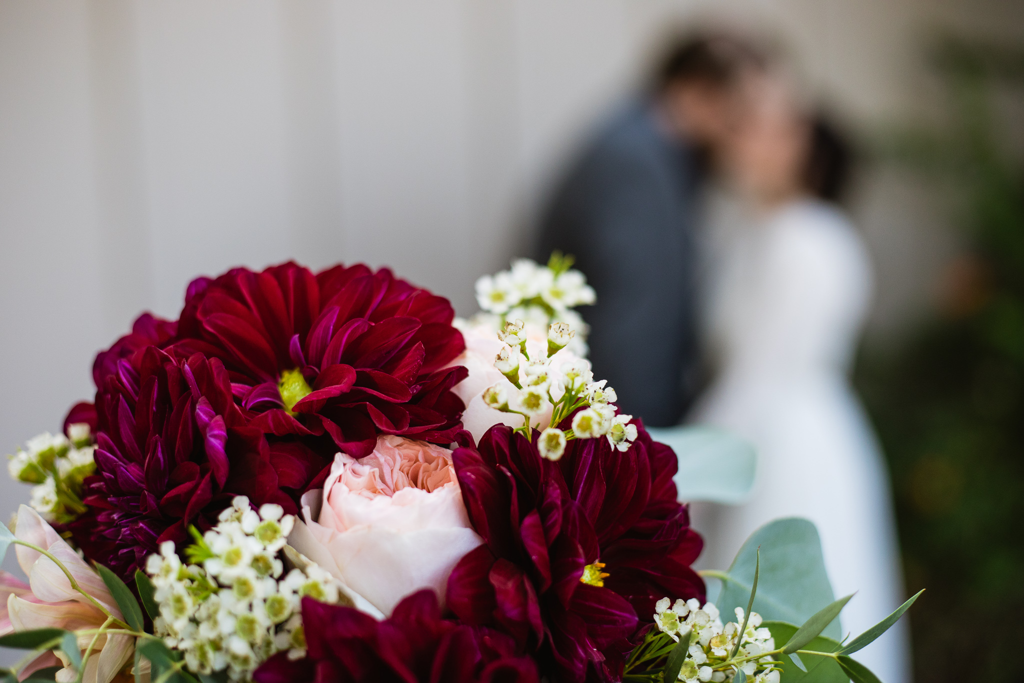 Burgundy pink and cream wedding bouquet with bride and groom kissing in the background.