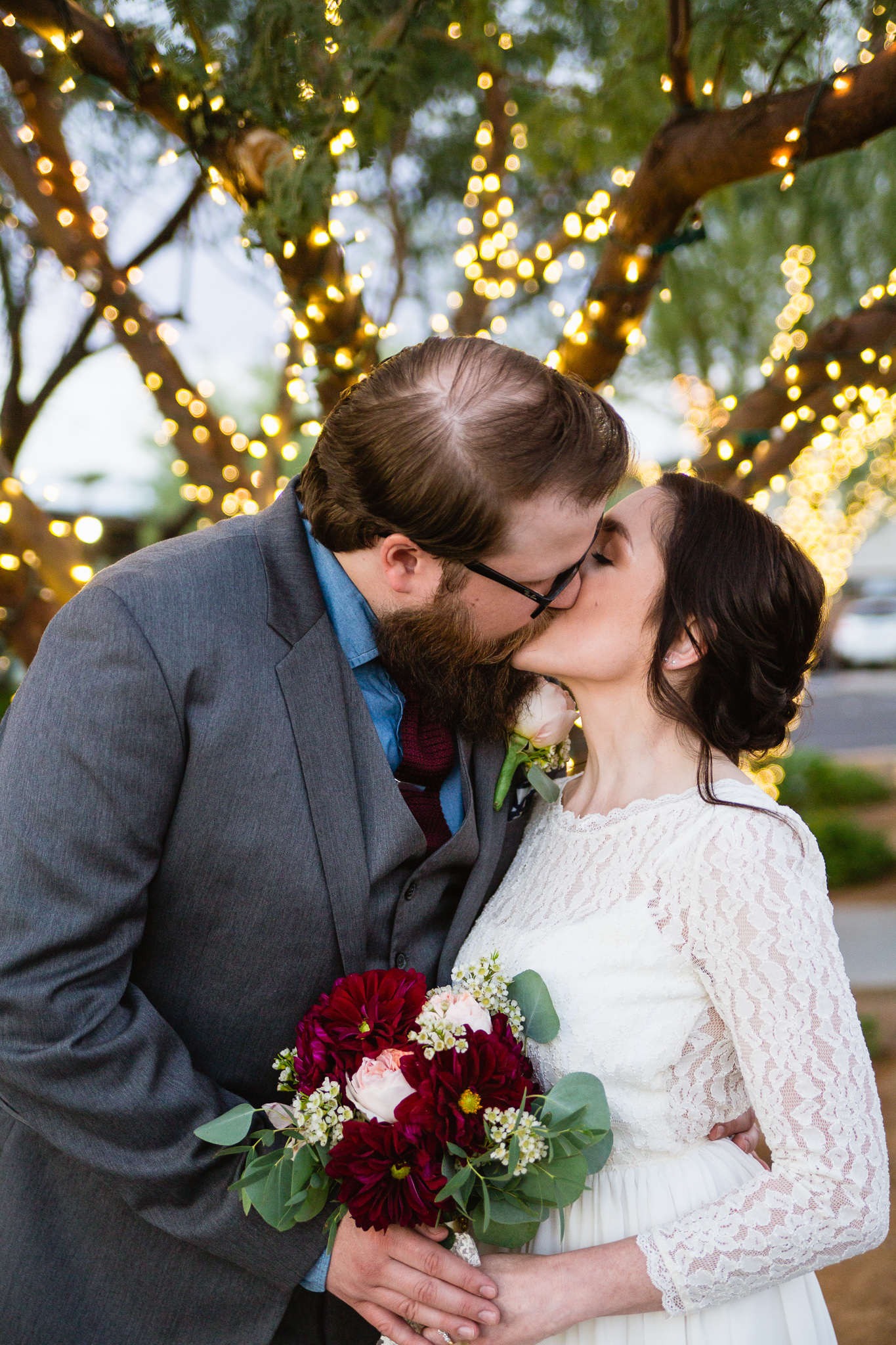 Vintage inspired bride and groom sharing a kiss in front of Christmas lights at their winter wedding.