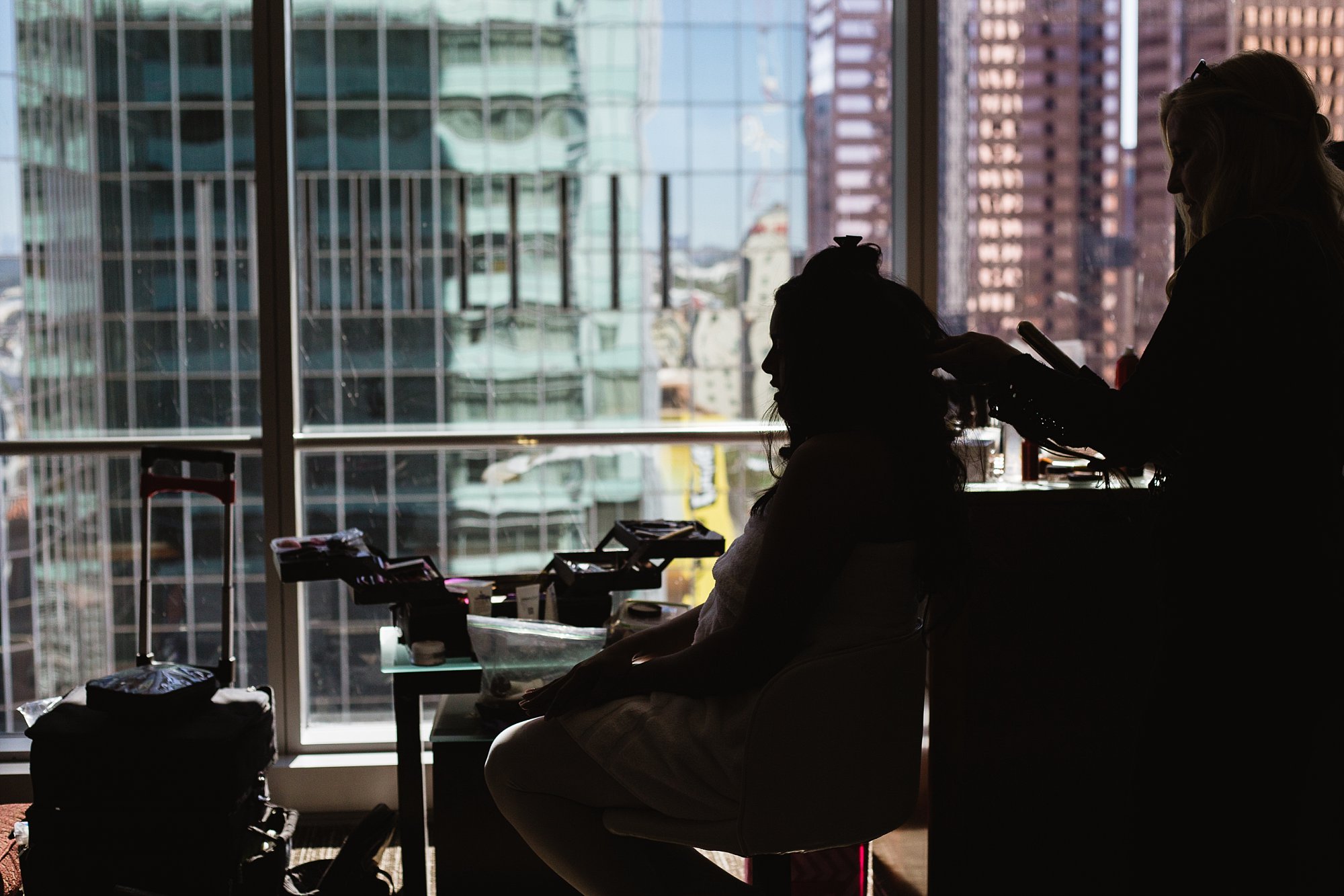 Silhouette image of bride getting her hair done with a view of the Skyscrapers of downtown Phoenix by wedding photographers PMA Photography.