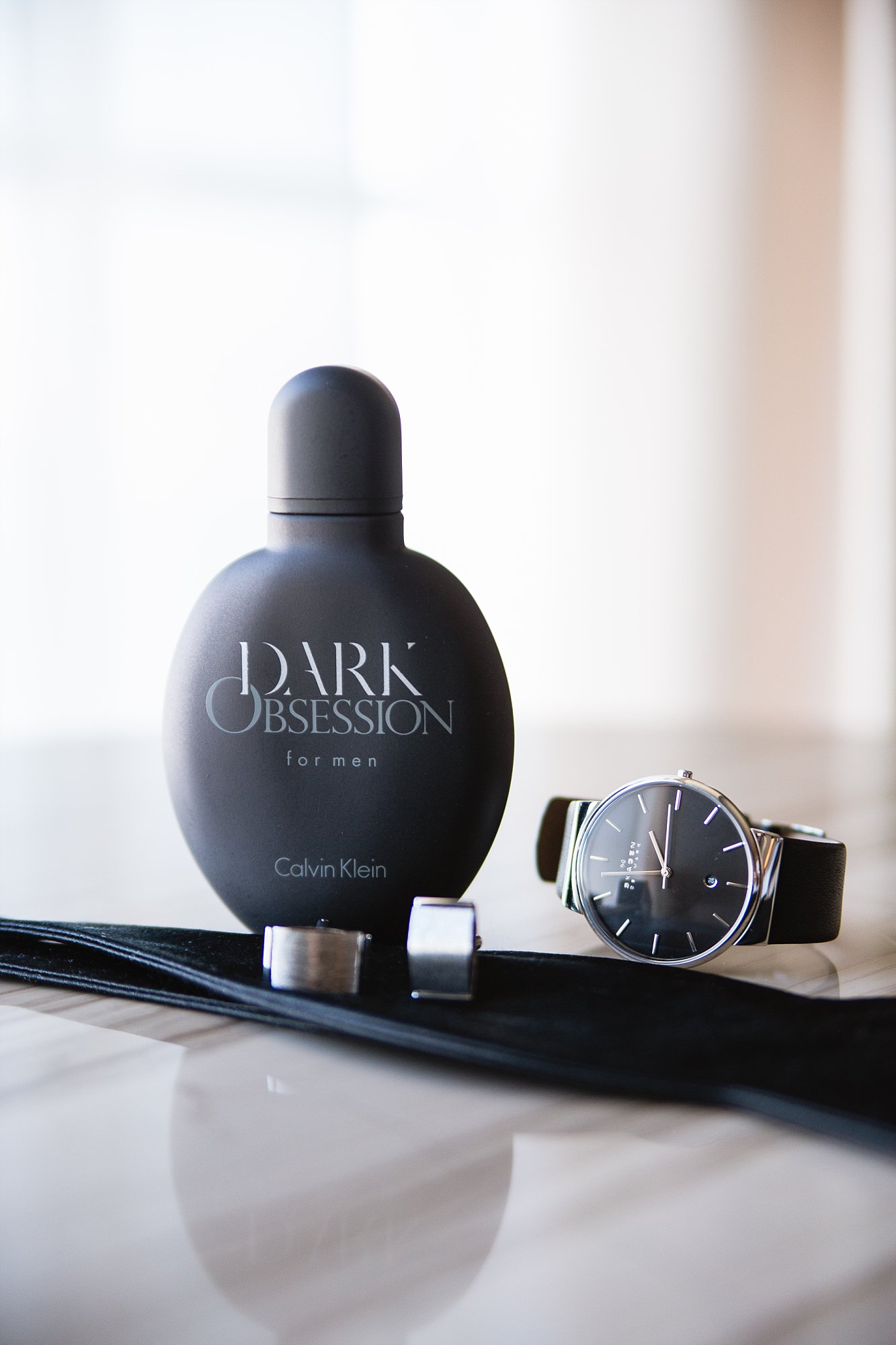 Detail image of groom's Dark Obsession cologne, black wedding watch, cuff links, and bow tie by Phoenix wedding photography PMA Photography.
