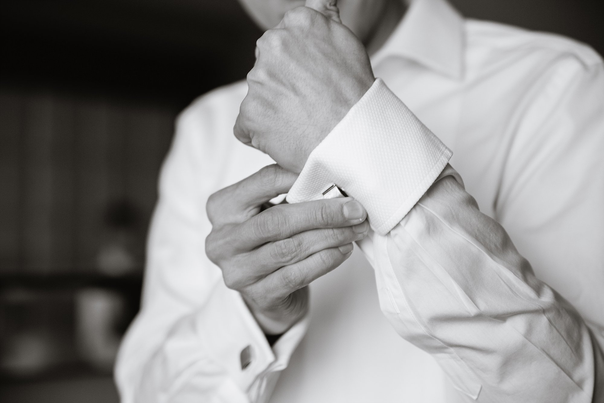 Black and white image of groom putting on his cuff links while getting ready for his wedding day by Phoenix wedding photographer PMA Photography.