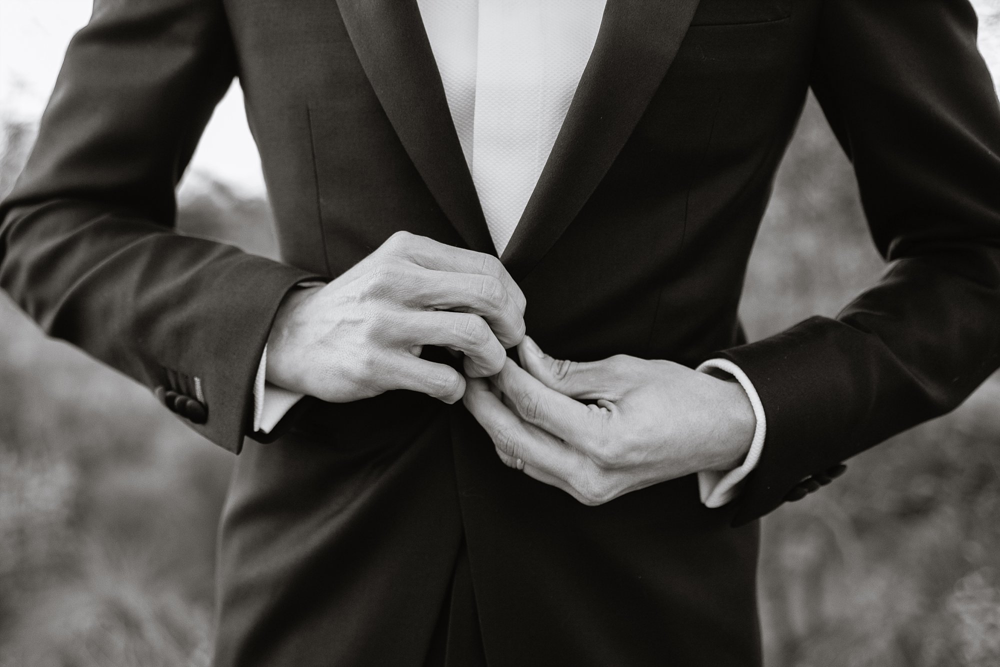 Black and white image of groom buttoning his tux jacket by Phoenix wedding photographer PMA Photography.
