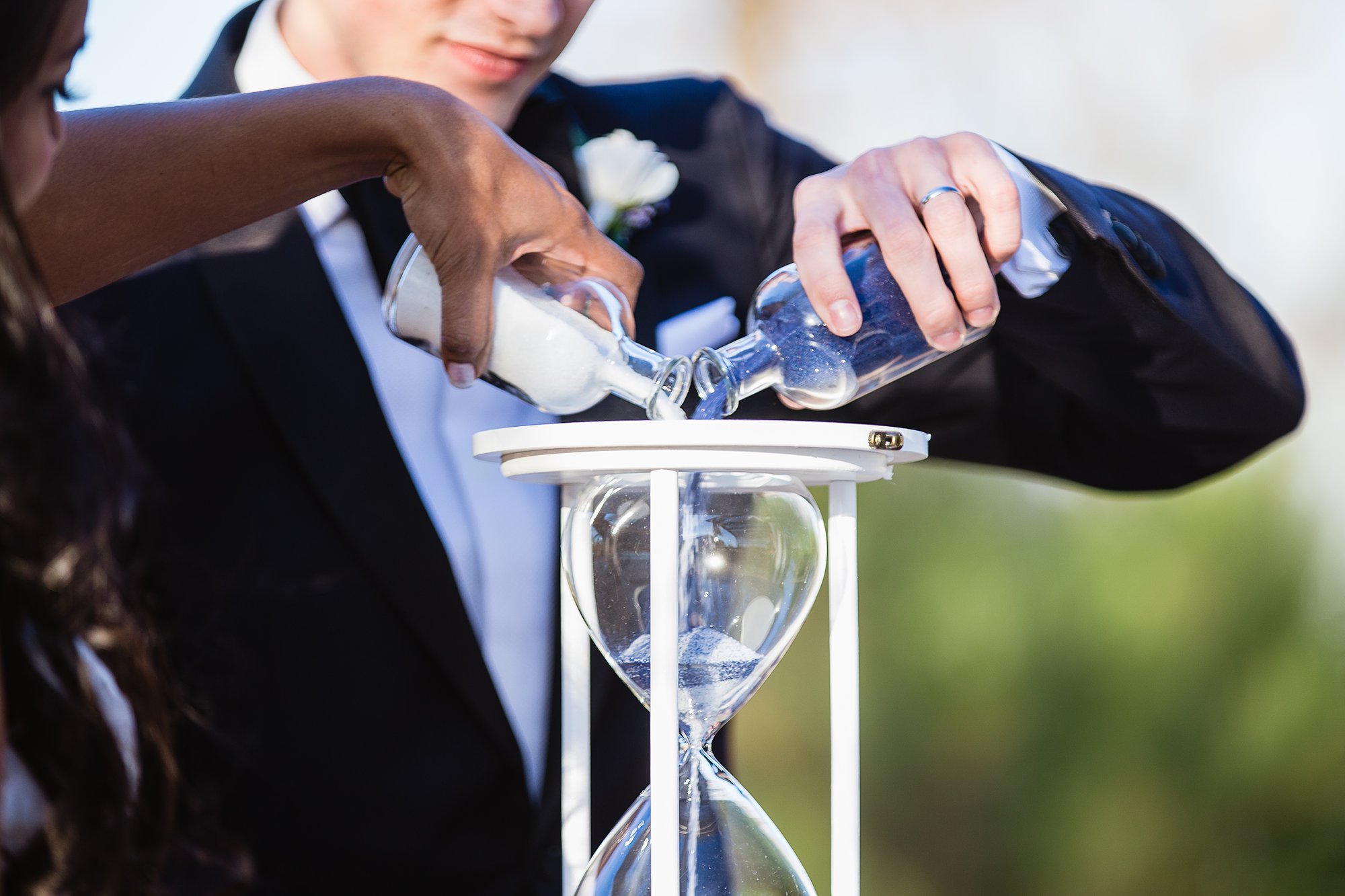 Bride and groom adding sand to an hour glass as their unity ceremony during wedding ceremony at the Rio Salado Audubon by Phoenix wedding photographers PMA Photography.