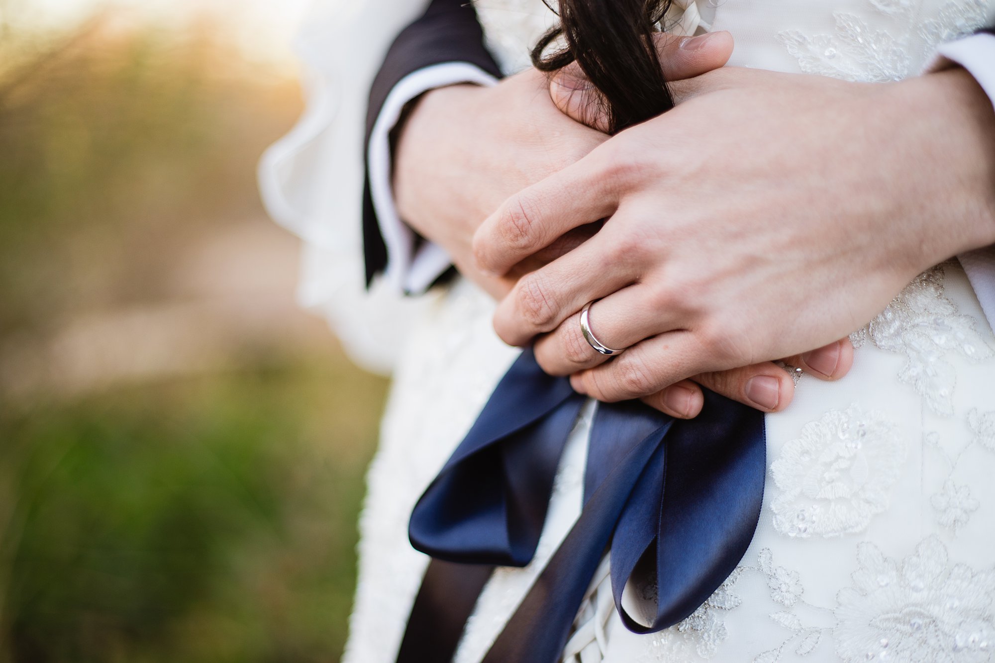 Detail image of groom's wedding ring as he wraps his arms around the bride by PMA Photography.