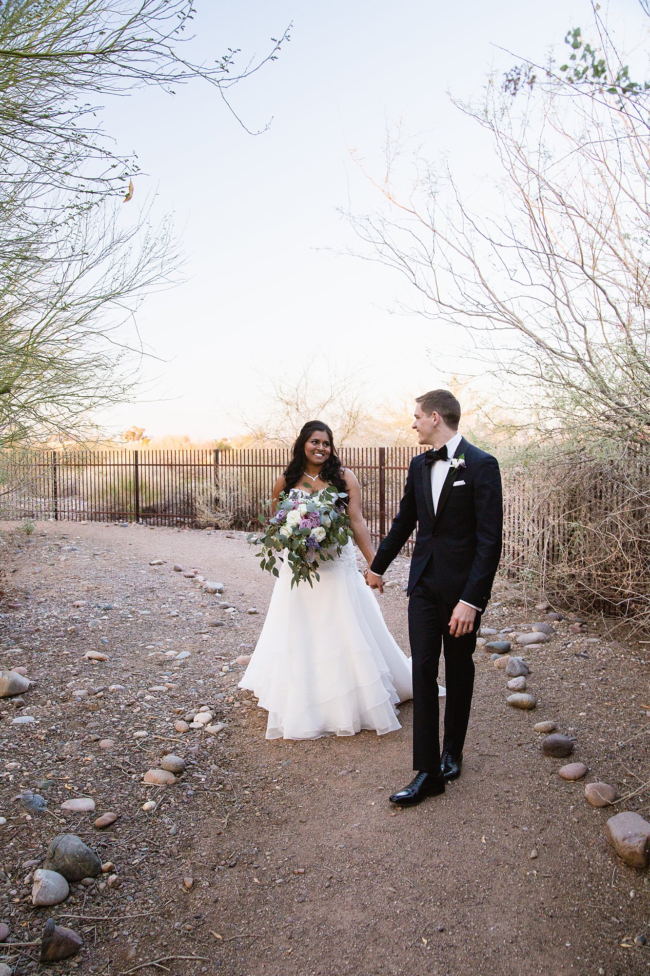 Groom leading the bride down a small desert trail at the Rio Salado Audubon center by Phoenix wedding photographer PMA Photography.