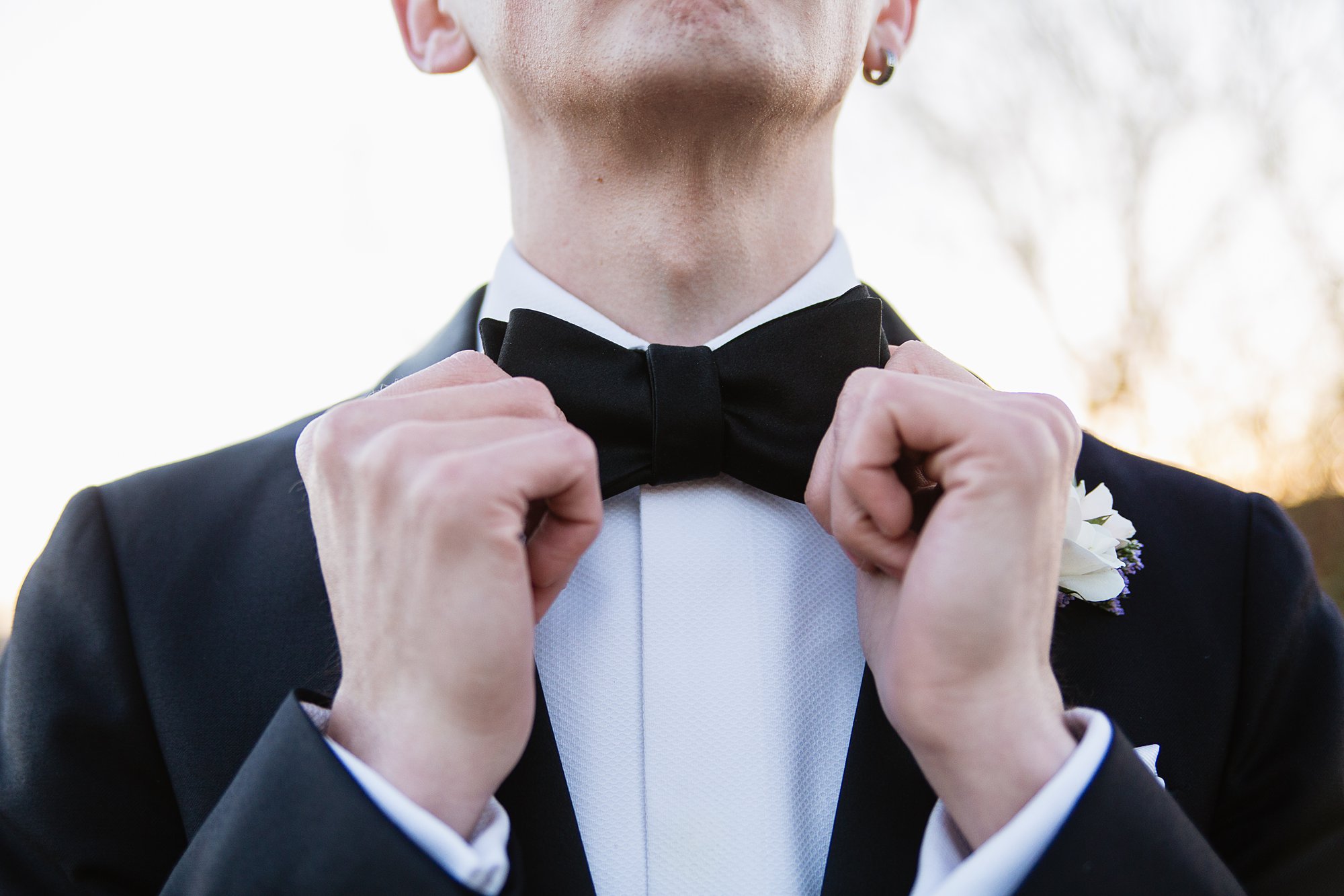 Groom adjusting his bow tie on his wedding day by photographer PMA Photography.