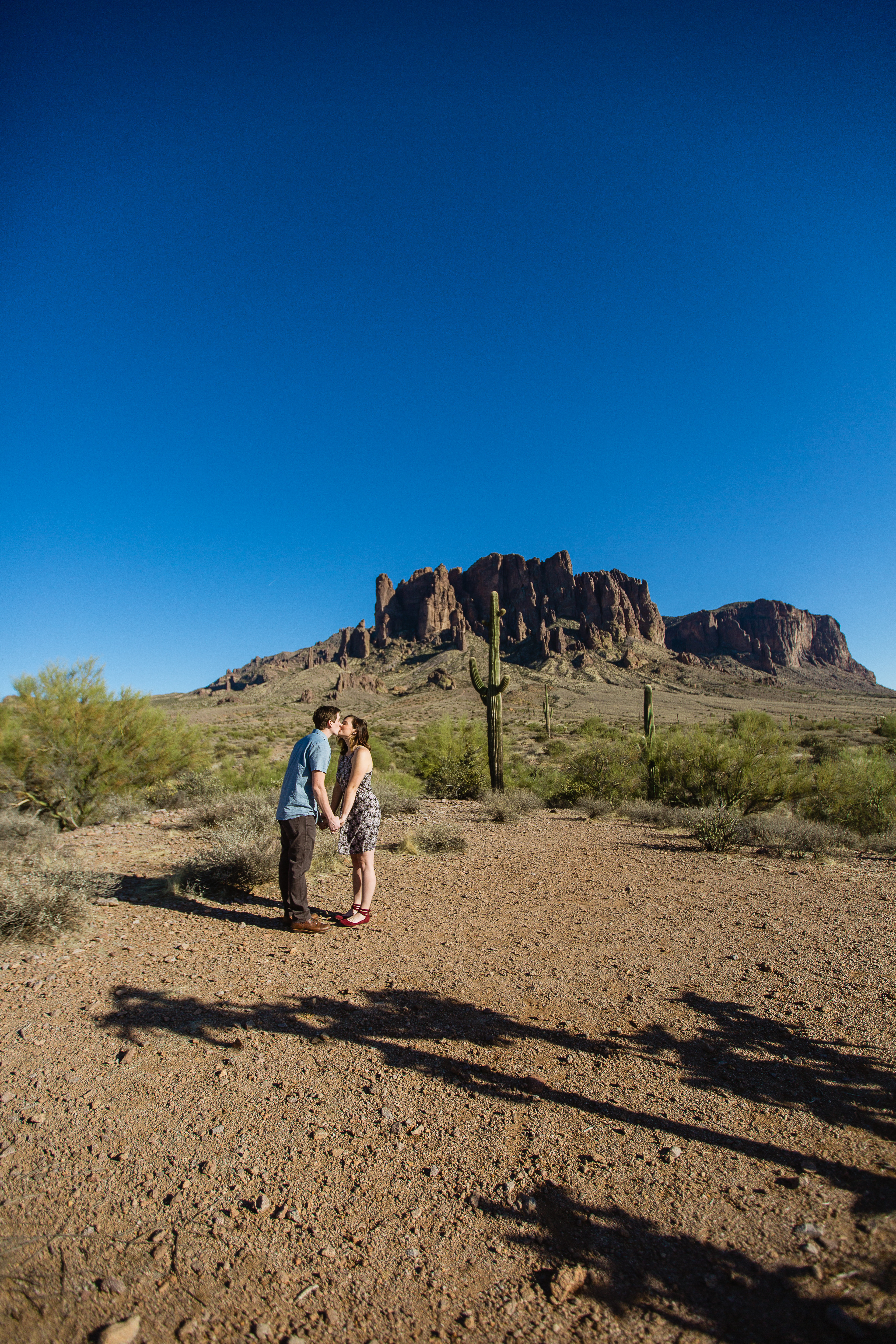 Couple standing in front of the superstition mountains at desert engagement session at Lost Dutchman State Park by wedding photographer PMA Photography.