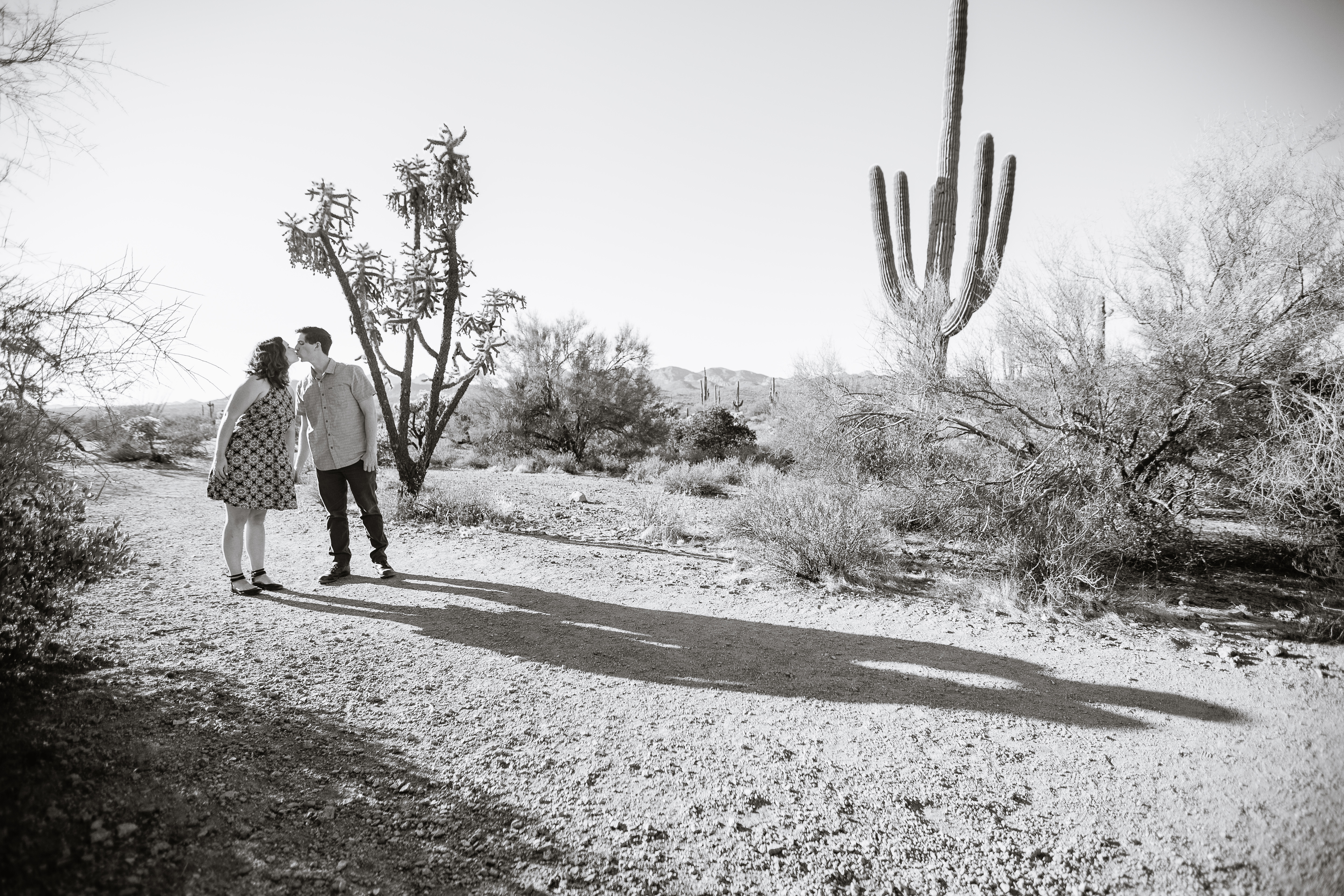 Black and white image of couple kissing with their shadows during desert engagement session at Lost Dutchman State Park by Phoenix wedding photographers PMA Photography.