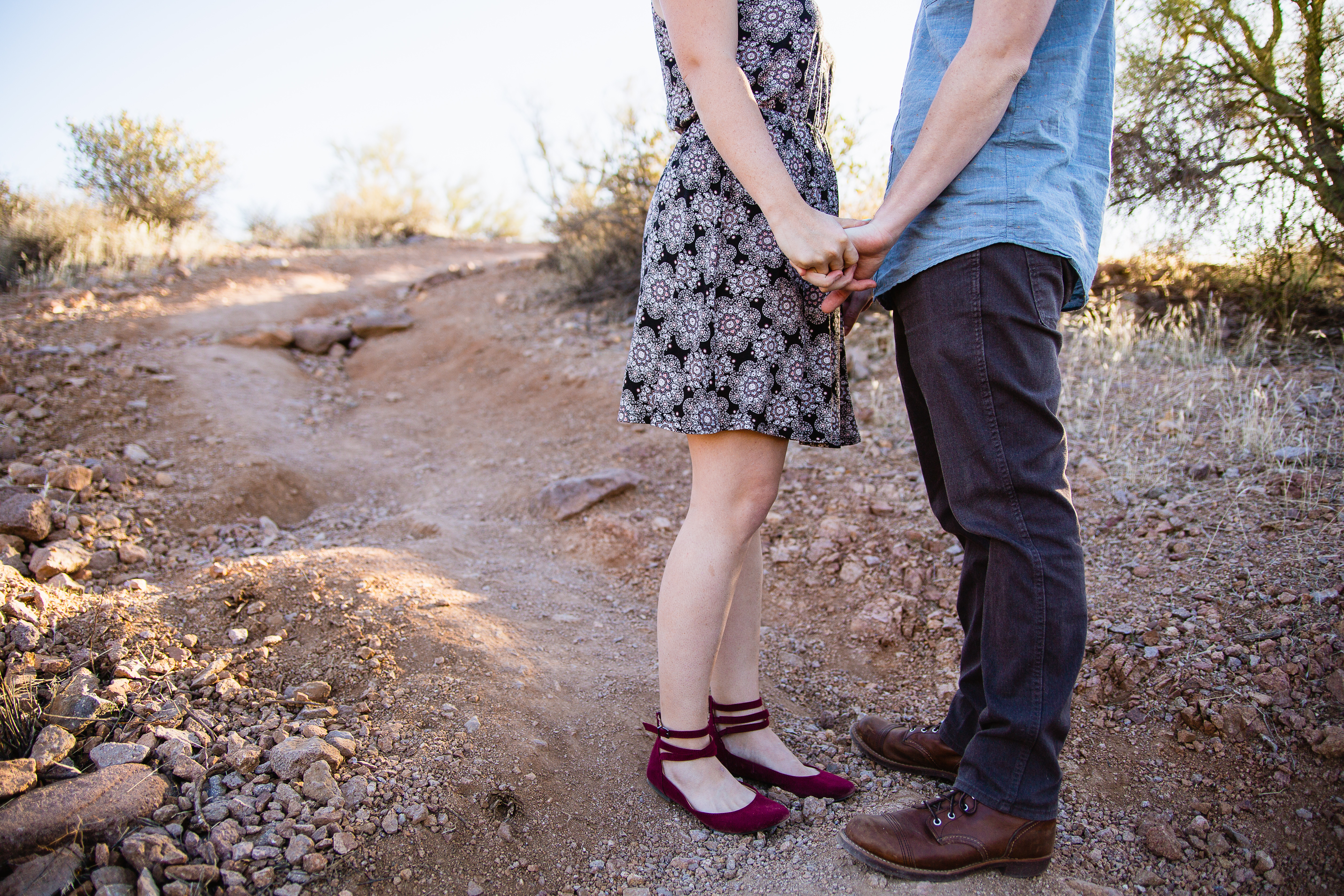 Image of couples outfits and they hold hands on a desert path during their Couple sharing one reason they love each other at desert engagement session at Lost Dutchman State Park by Phoenix engagement photographers PMA Photography.