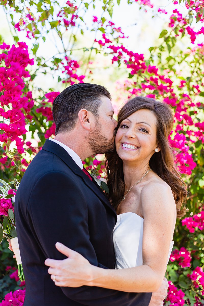 Groom kissing bride's cheek in front of bogainvillea by Arizona wedding photographer PMA Photography.
