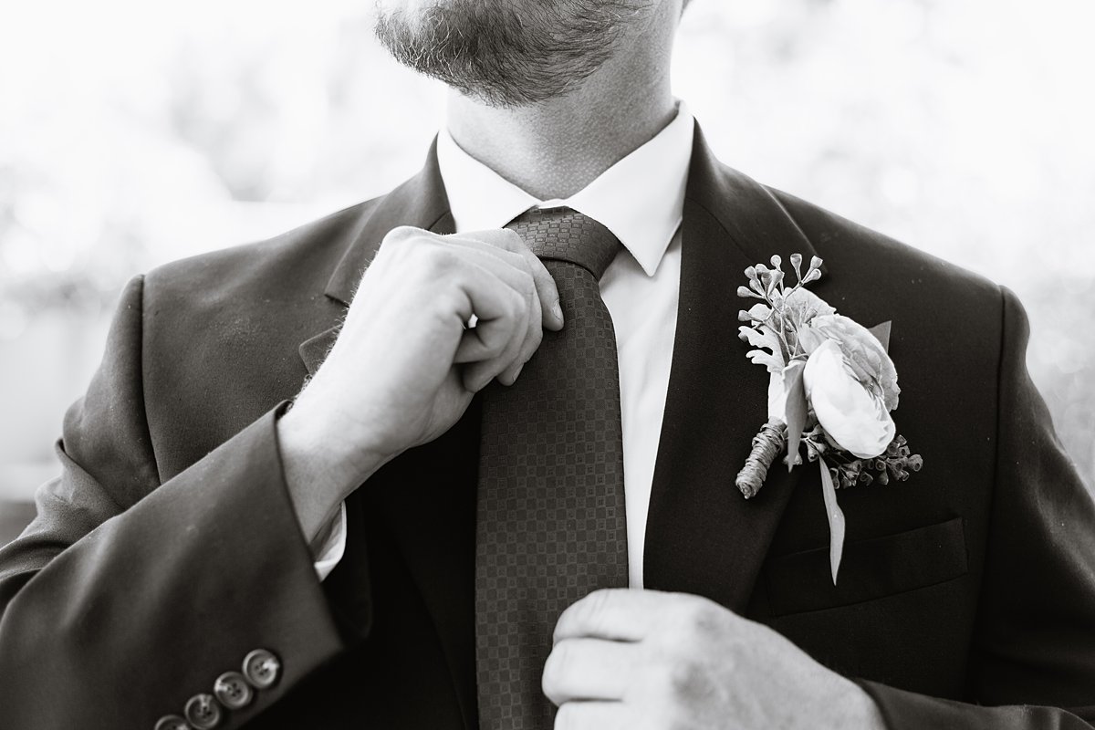 Black and white image of groom adjusting his tie by wedding photographer PMA Photography.