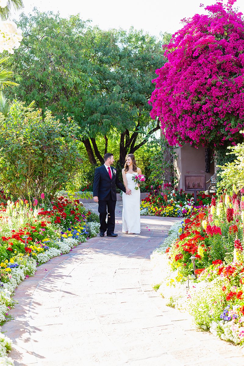 Classic style bride and groom walk through a colorful garden at Hermosa Inn by Phoenix wedding photographers PMA Photography.