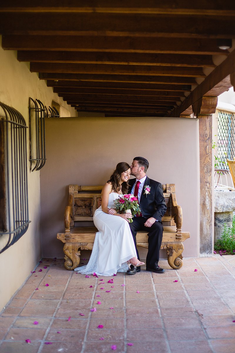 Groom kissing bride on a vintage style wooden bench at Hermosa Inn by Phoenix wedding photographer PMA Photography.