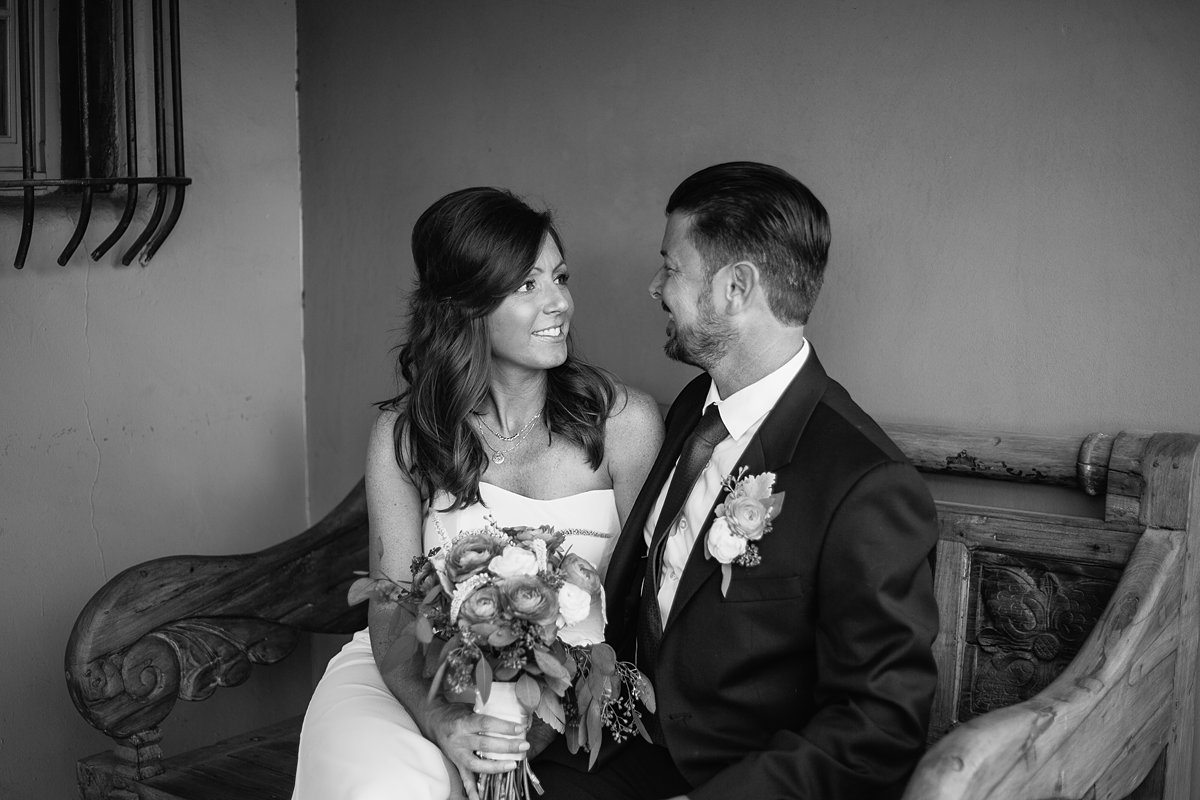 Black and white image of bride and groom sitting on a vintage style wooden bench at Hermosa Inn by Arizona wedding photographer PMA Photography.