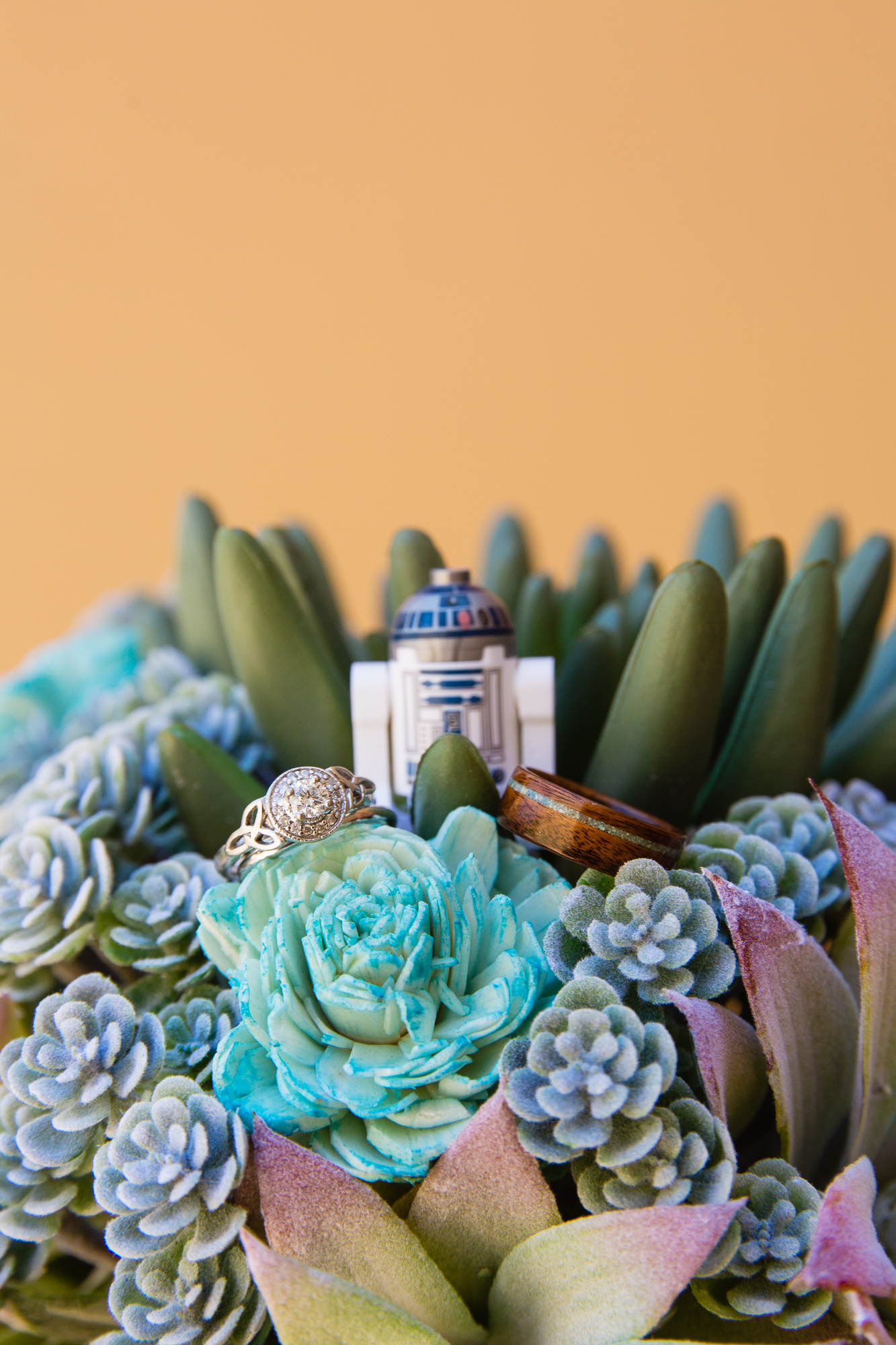 Bride and groom's wedding rings in a wood flower and succulent wedding bouquet with R2D2 for a Star Wars wedding by Arizona wedding photographer PMA Photography.
