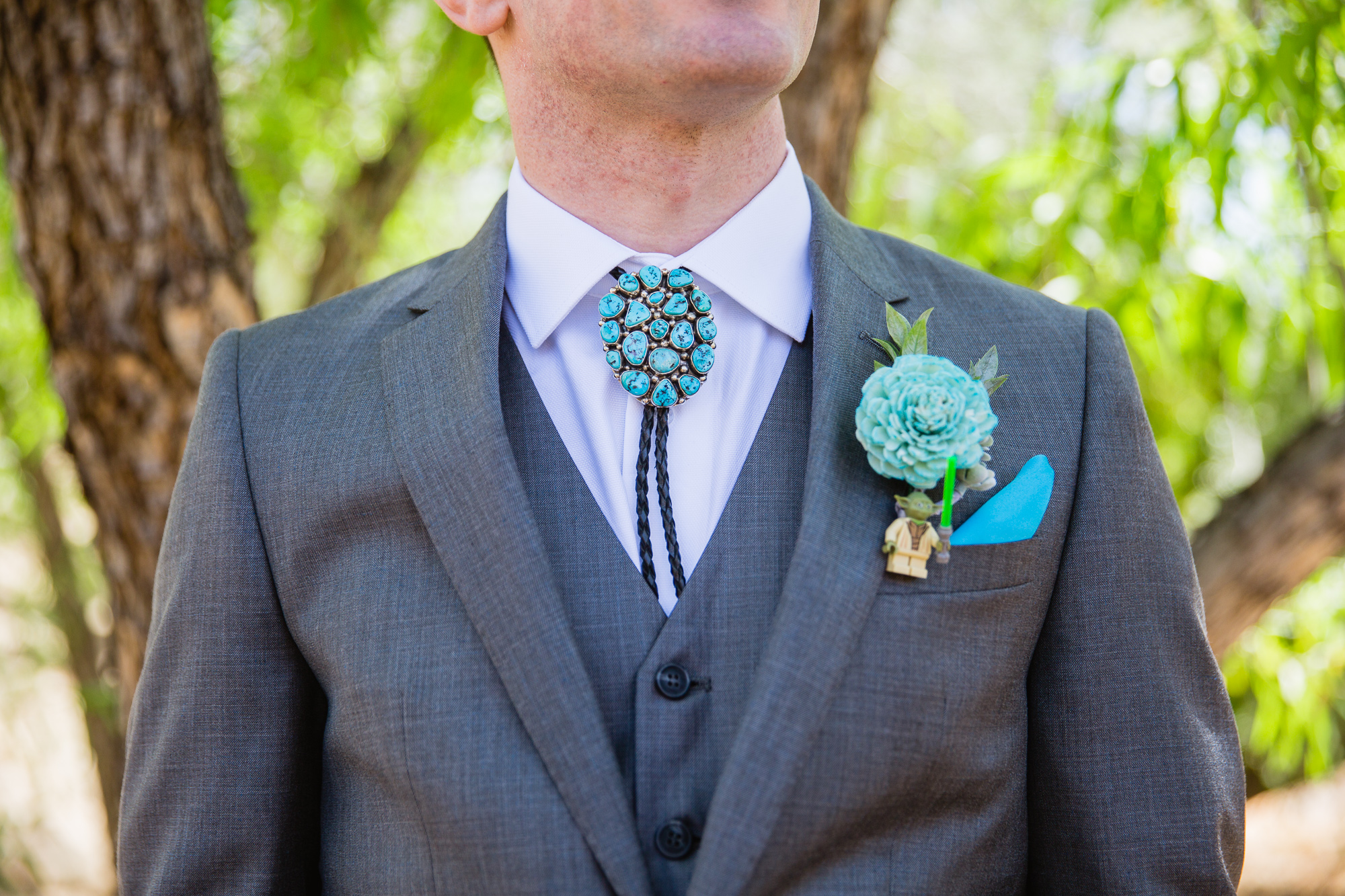 Groom in a grey suit with a turquoise bolo tie and a lego Star Wars boutonniere by Phoenix wedding photographers PMA Photography.
