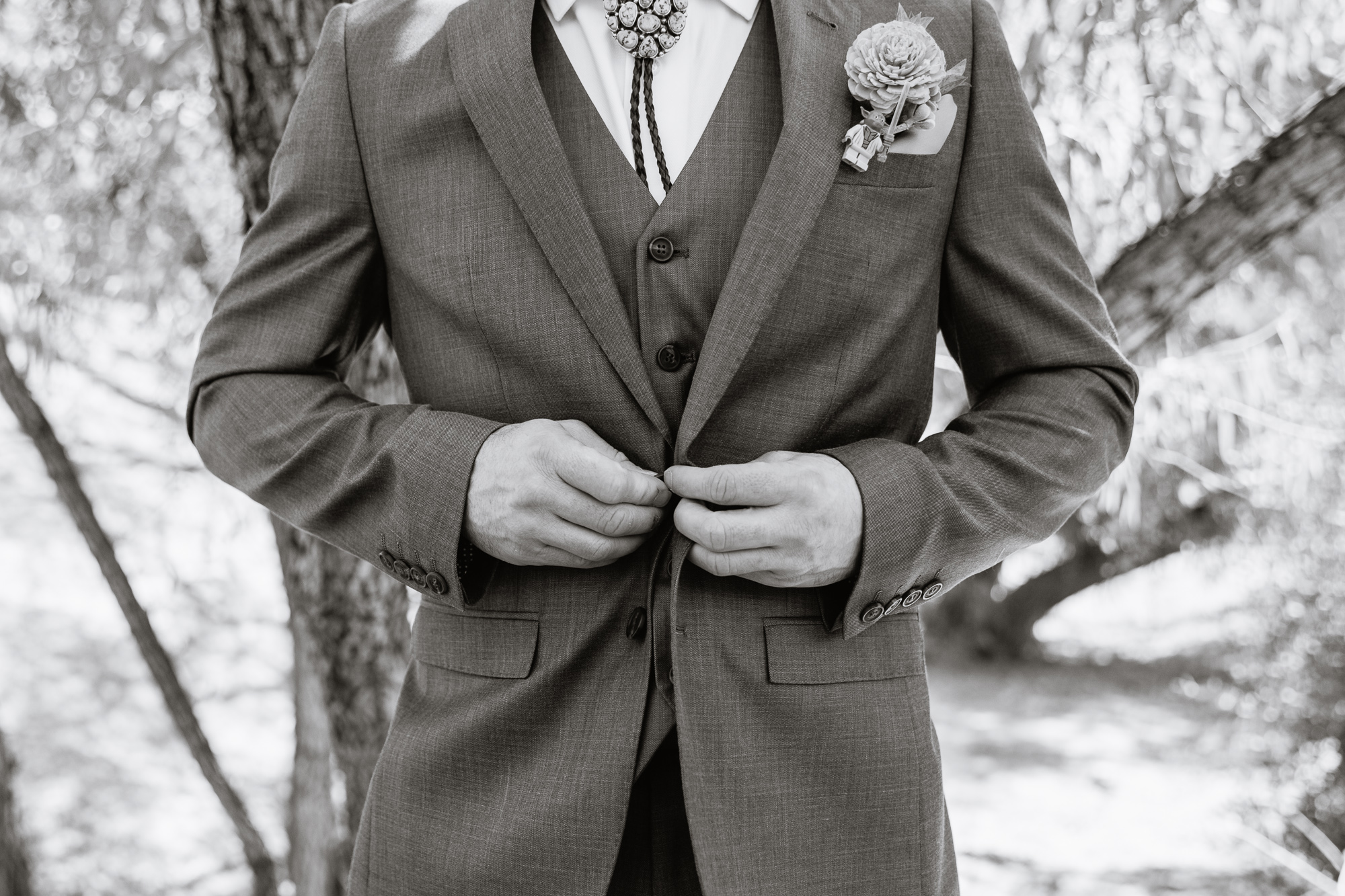 Black and white image of groom buttoning his suit jacket by Arizona wedding photographer PMA Photography.