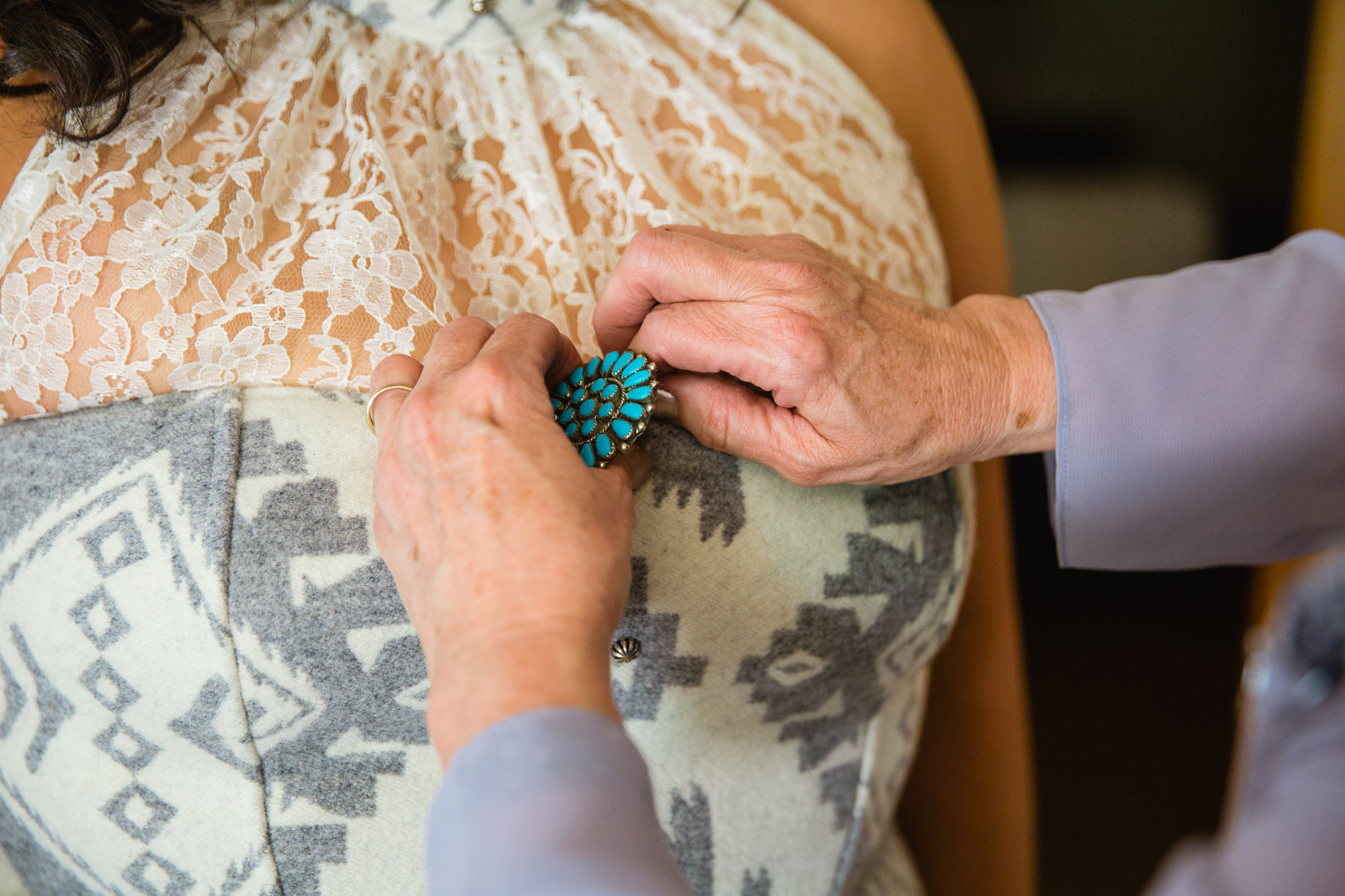 Mother of the bride pinning a turquoise broach on the bride's wedding dress by Phoenix wedding photographer PMA Photography.