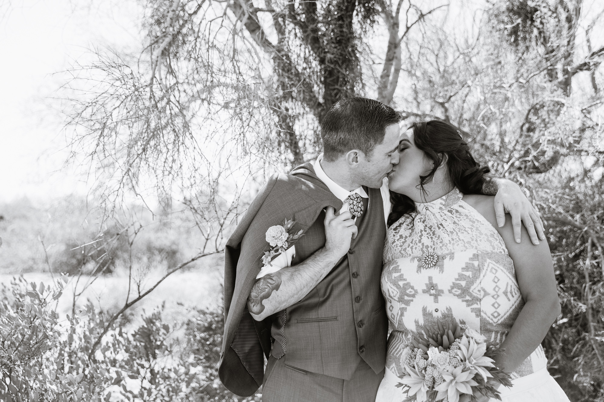 Black and white image of bride and groom kissing in the Arizona desert by wedding photographer PMA Photography.