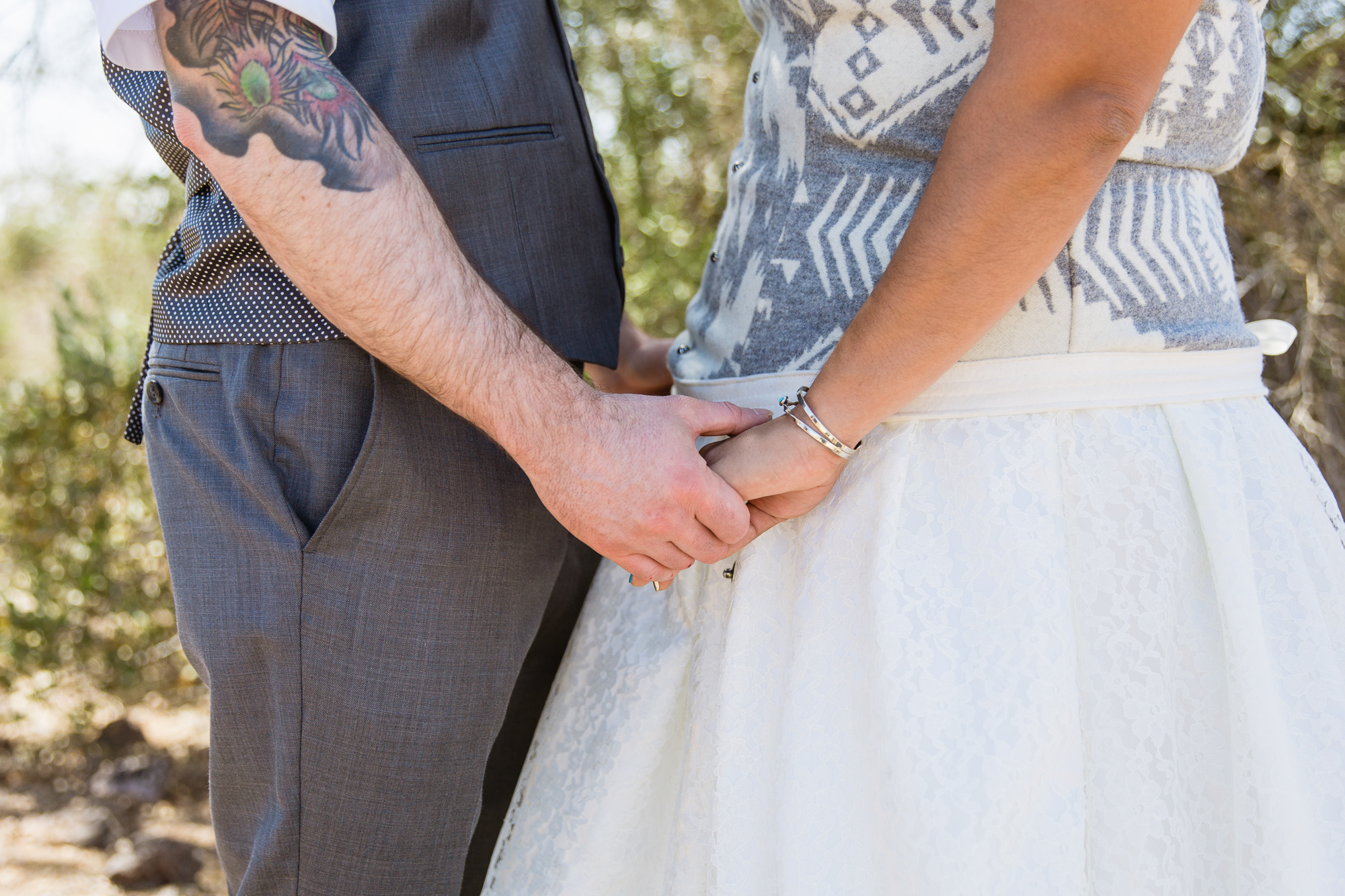 Close up image of tattooed groom and Navajo bride holding hands by PMA Photography.