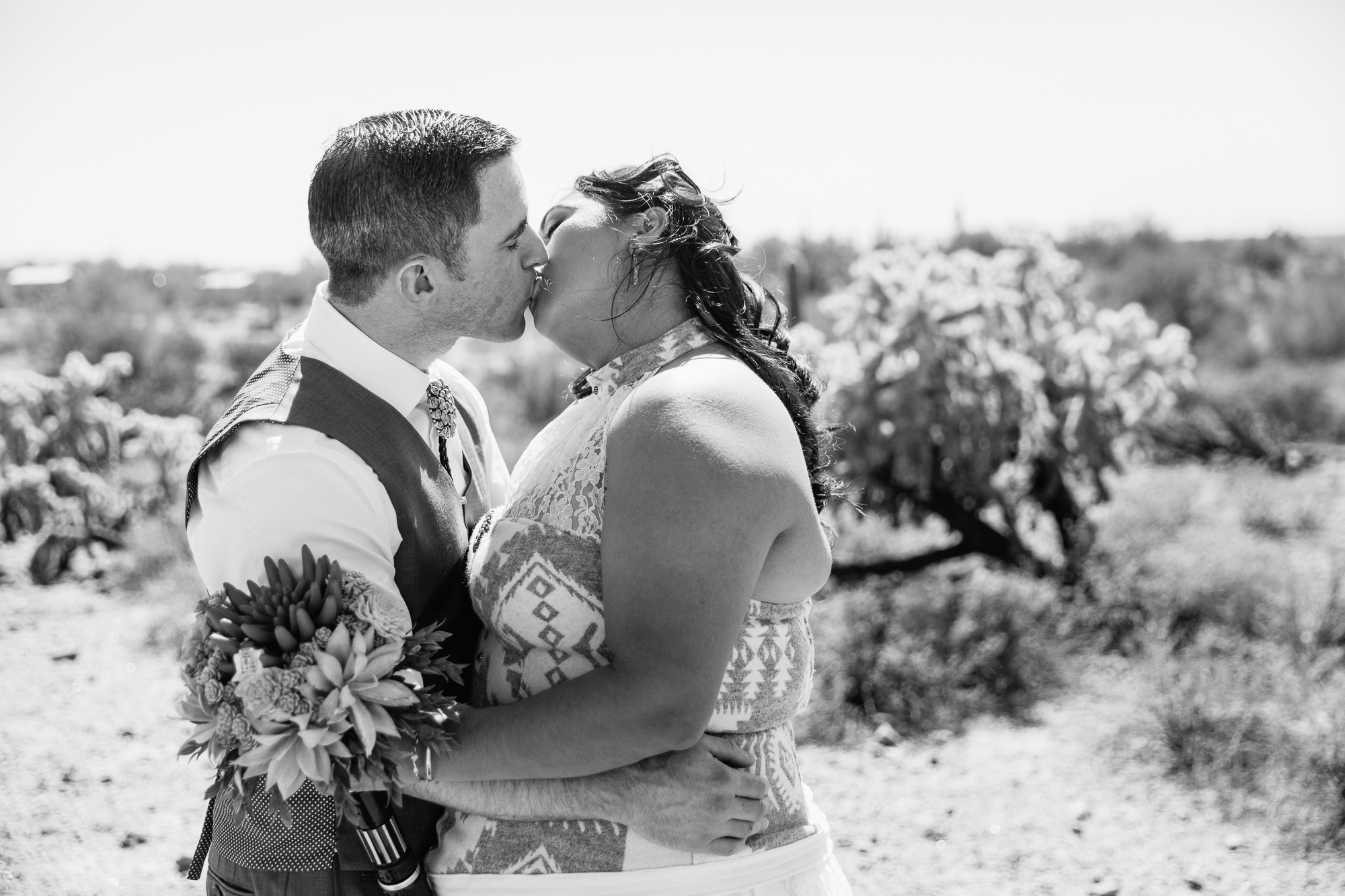 Black and white image of bride and groom kissing in the Arizona desert at Lost Dutchman State Park by wedding photographers PMA Photography.