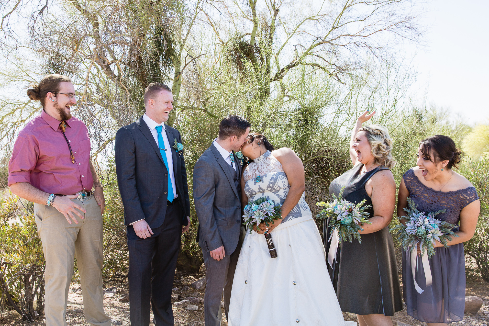 Bridal party getting excited while bride and groom kiss by Arizona wedding photographers PMA Photography.