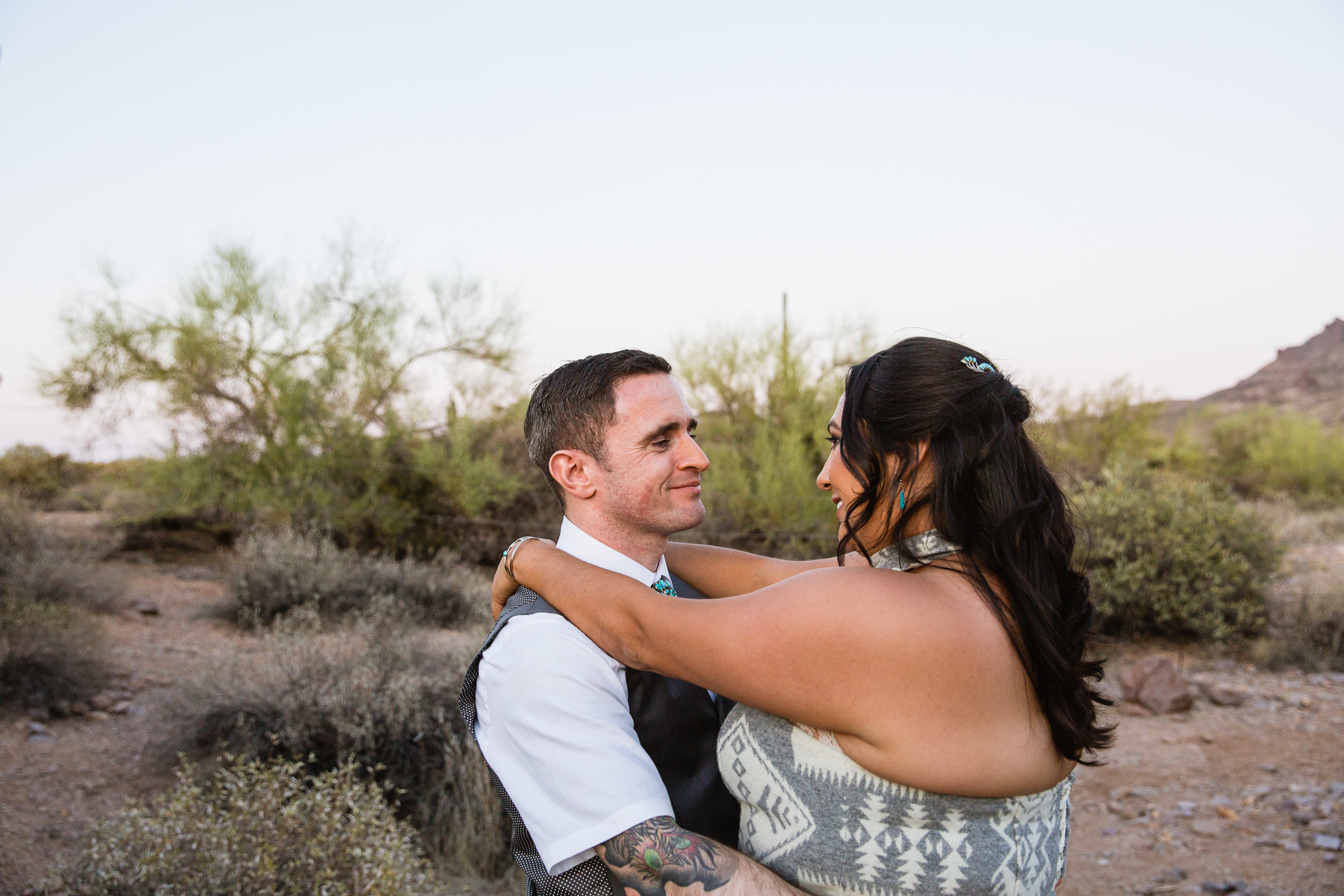 Tattooed groom looking at his bride at the superstition mountains at Lost Dutchman state park by Arizona wedding photographer PMA Photography.