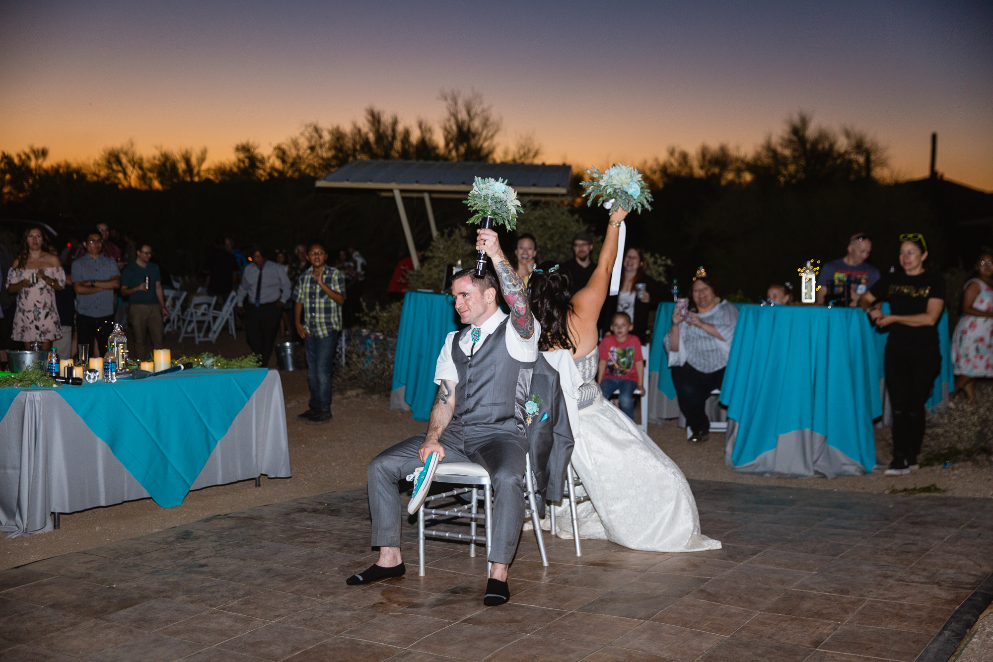 Bride and groom play the newlywed shoe game with turquoise converse and bouquets at their wedding reception by PMA Photography.